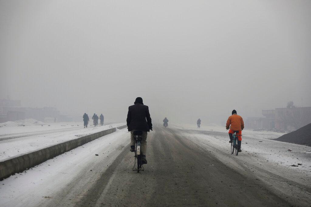 Los hombres afganos andan en bicicleta durante una densa niebla en Kabul, Afganistán.