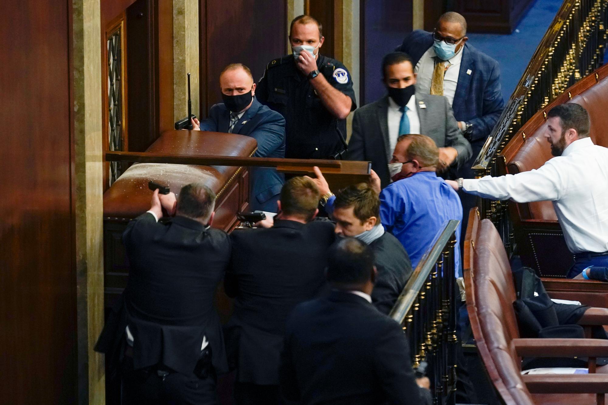 La policía del Capitolio de Estados Unidos con armas en la mano se para cerca de una puerta con barricadas mientras los manifestantes intentan irrumpir en la Cámara de la Cámara en el Capitolio de Estados Unidos el miércoles 6 de enero de 2021 en Washington.