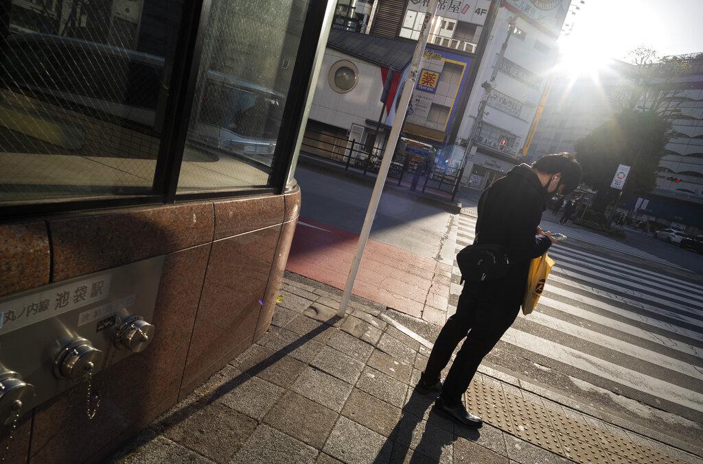 Un hombre portando una mascarilla y revisando su celular aguarda para cruzar una calle en Tokio, una ciudad que suele vivir a un ritmo frenético pero que muestra otra cara en medio del decreto de estado de emergencia por el COVID-19 (AP Photo/Hiro Komae)