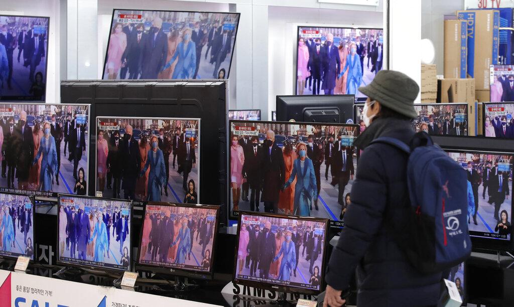 Un hombre pasa frente a una tienda que vende televisores en los que se proyecta el acto de toma de posesión del presidente Joe Biden (AP Photo/Lee Jin-man)
