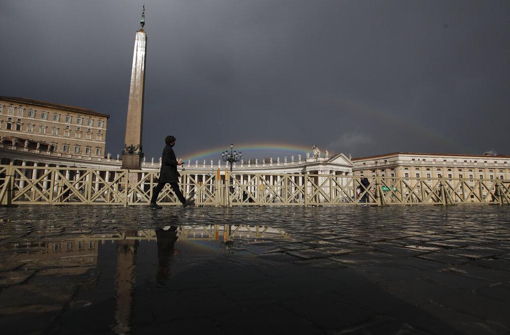Un hombre camina por la Plaza de San Pedro en el Vaticano, mientras un pequeño arcoíris se levanta detrás de la edificación  (AP Photo/Alessandra Tarantino)