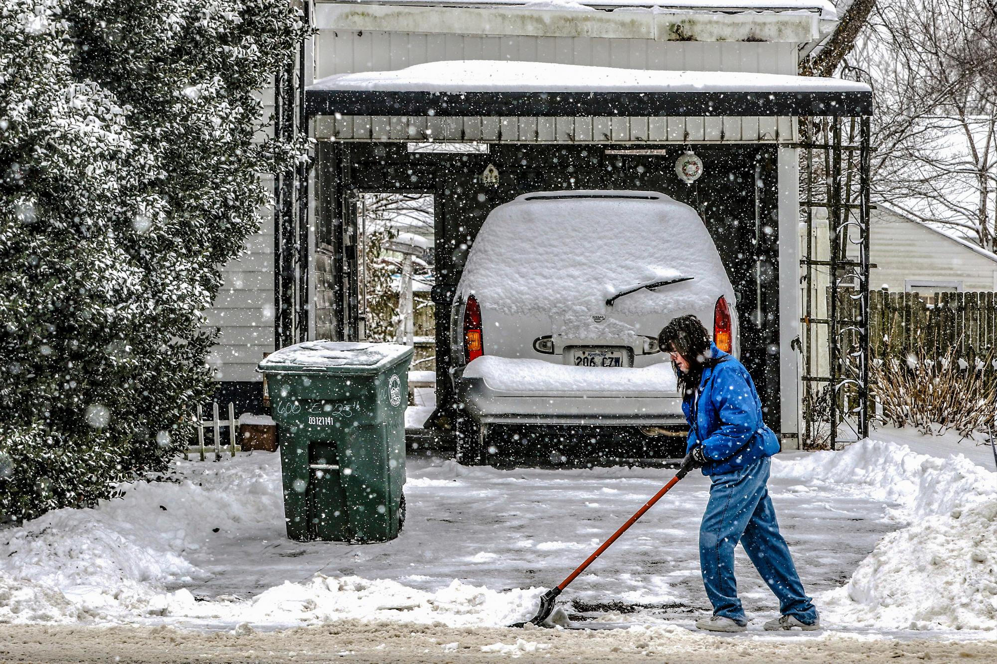Jennifer Spence ayuda a un amigo a limpiar el camino de entrada mientras cae una nevada ligera, el jueves 18 de febrero de 2021 en Owensboro, Kentucky. (Greg Eans/The Messenger-Inquirer via AP)