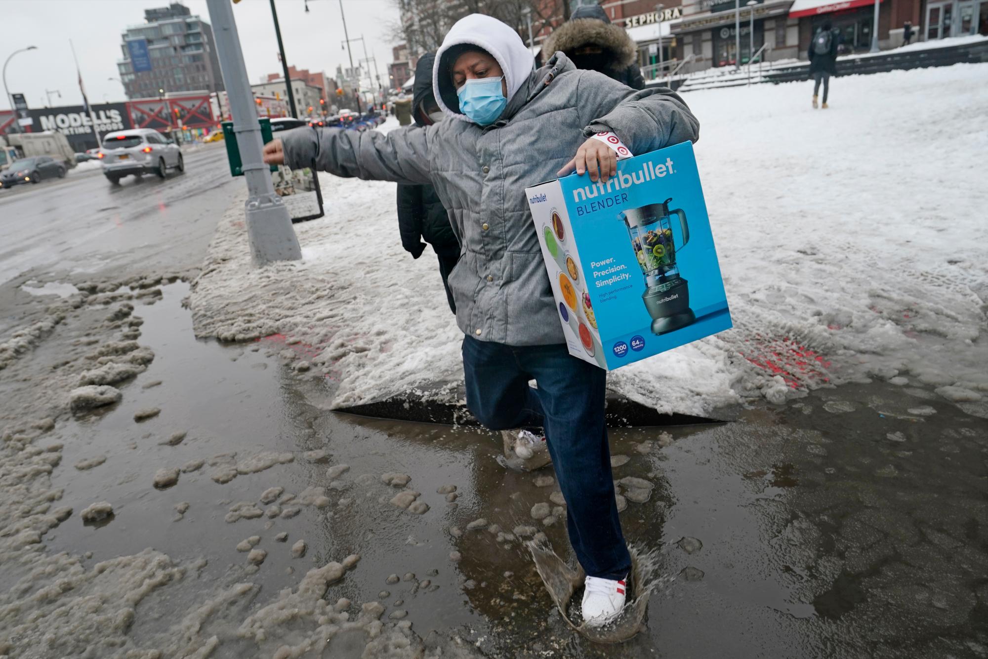 Un hombre salpica en un charco de agua fangosa en una intersección en el centro de Brooklyn después de que varias pulgadas de nieve seguidas de aguanieve y lluvia helada cayeran sobre el área el jueves 18 de febrero de 2021 en Nueva York. (AP Photo/Kathy Willens)