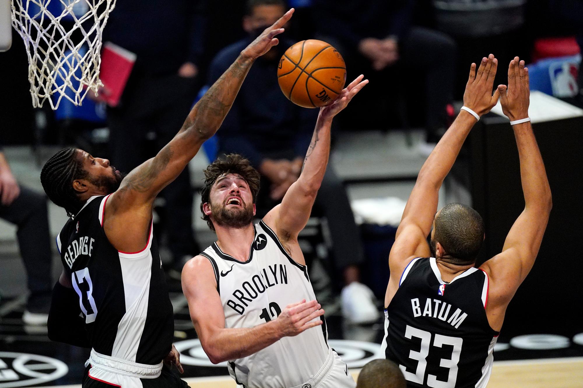 El alero de los Brooklyn Nets, Joe Harris, en el centro, dispara cuando los Angeles Clippers escolta a Paul George, a la izquierda, y el alero Nicolas Batum defienden durante la segunda mitad de un juego de baloncesto de la NBA el domingo 21 de febrero de 2021 en Los Ángeles.