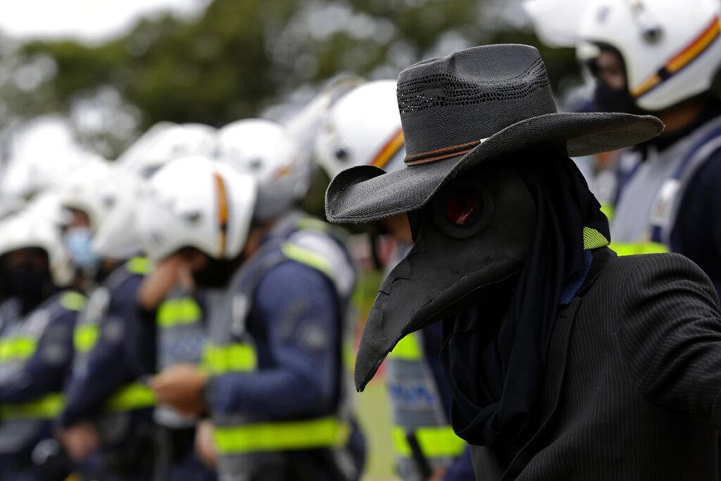 Un manifestante disfrazado con el traje del ave que recuerda a la peste, durante la protesta ante la imposición de una cuarentena de dos semanas que busca detener el crecimiento de la pandemia del COVID-19 en Brasilia, capital de Brasil.  (AP Photo/Eraldo Peres)