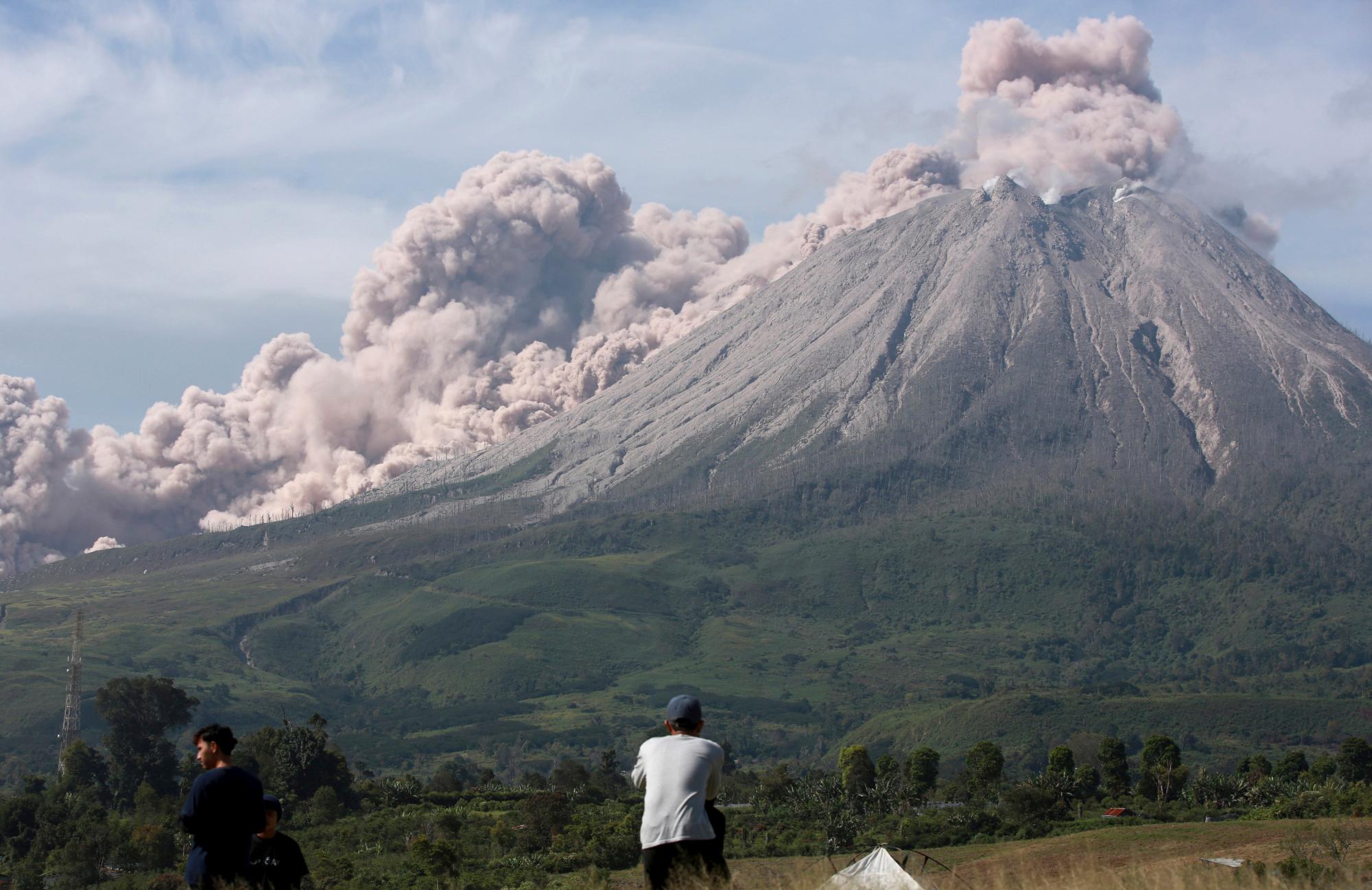 La gente observa cómo el monte Sinabung arroja materiales volcánicos durante una erupción en Karo, en el norte de Sumatra, Indonesia, el jueves 11 de marzo de 2021. El volcán desató una avalancha de abrasadoras nubes de gas que fluían por sus laderas durante la erupción del jueves. No se informó de víctimas.
