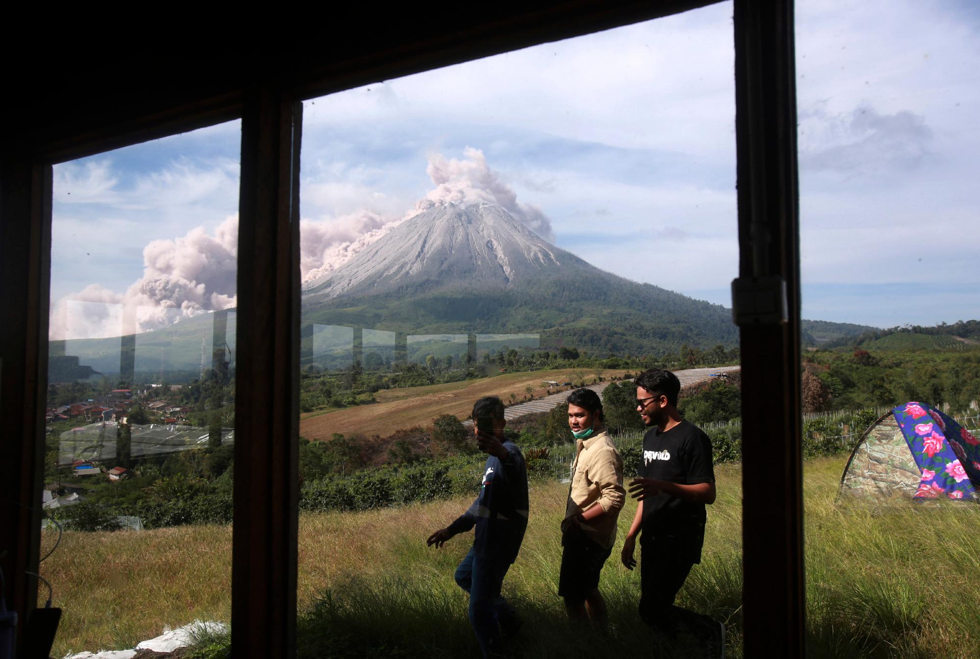 La gente pasa caminando mientras el Monte Sinabung arroja materiales volcánicos durante una erupción en Karo, en el norte de Sumatra, Indonesia, el jueves 11 de marzo de 2021. El volcán de 2.600 metros (8.530 pies) desató una avalancha de abrasadoras nubes de gas que fluían por sus laderas durante erupción el jueves. No se informó de víctimas.
