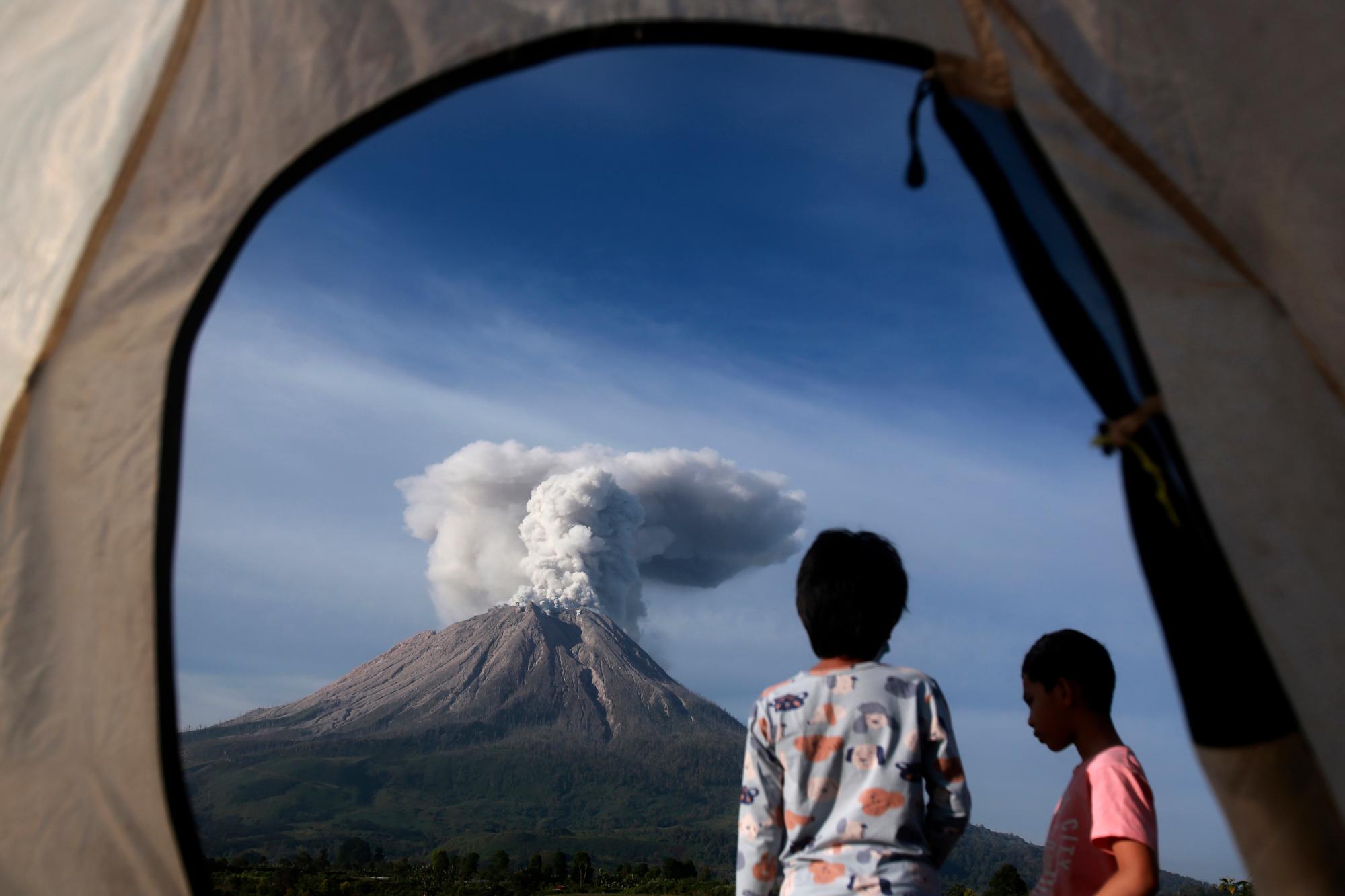 Los campistas son vistos desde la apertura de una carpa mientras observan la erupción del Monte Sinabung en Karo, en el norte de Sumatra, Indonesia, el jueves 11 de marzo de 2021. El volcán de 2.600 metros (8.530 pies) desató una avalancha de abrasadoras nubes de gas que fluían por su pendientes durante la erupción del jueves. No se informó de víctimas.