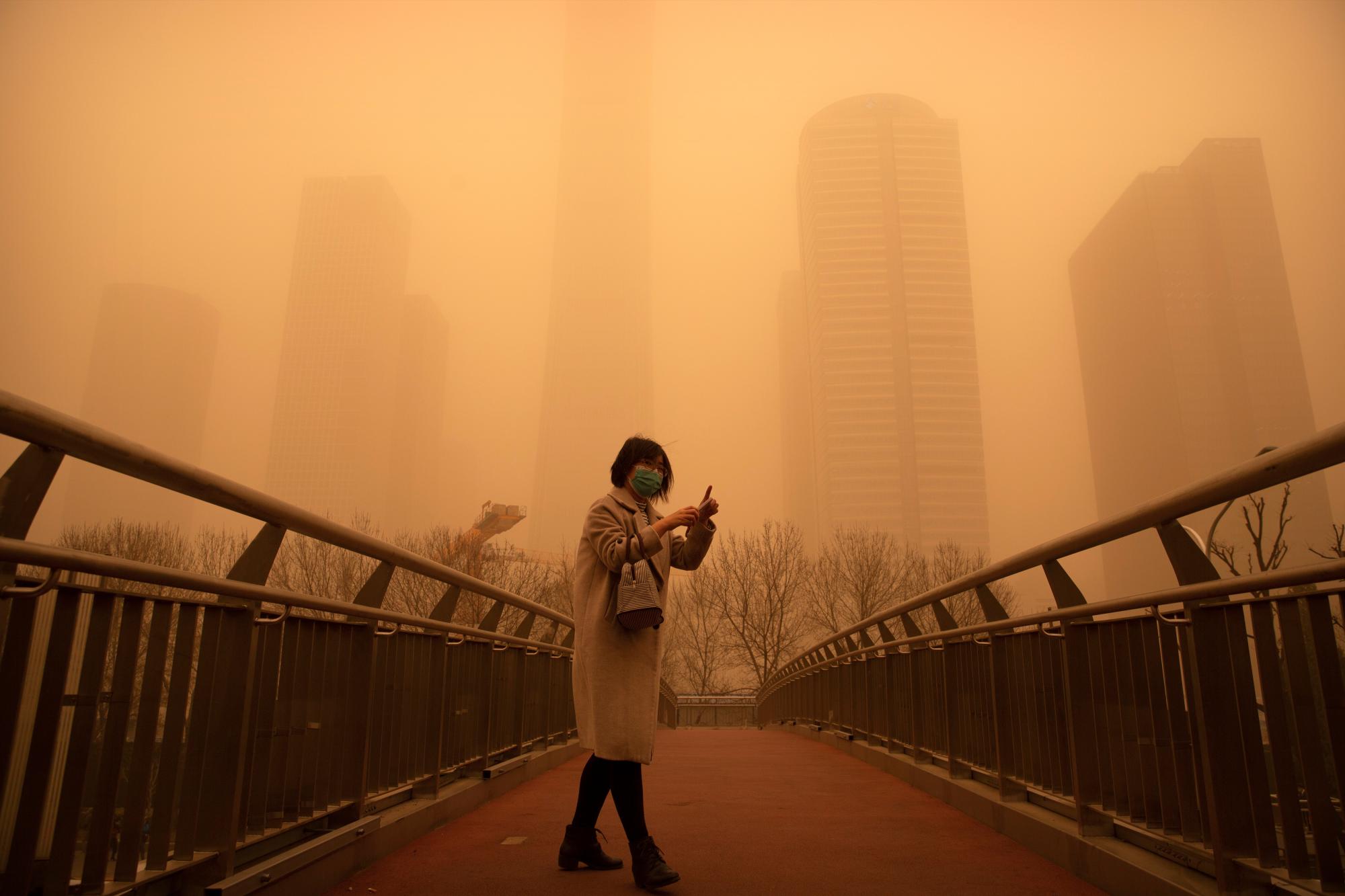Una mujer camina a lo largo de un puente peatonal en medio de una tormenta de arena durante la hora pico de la mañana en el distrito comercial central de Beijing, el lunes 15 de marzo de 2021. La tormenta de arena trajo una neblina teñida a los cielos de Beijing y elevó los índices de calidad del aire el lunes. (AP Photo/Mark Schiefelbein)