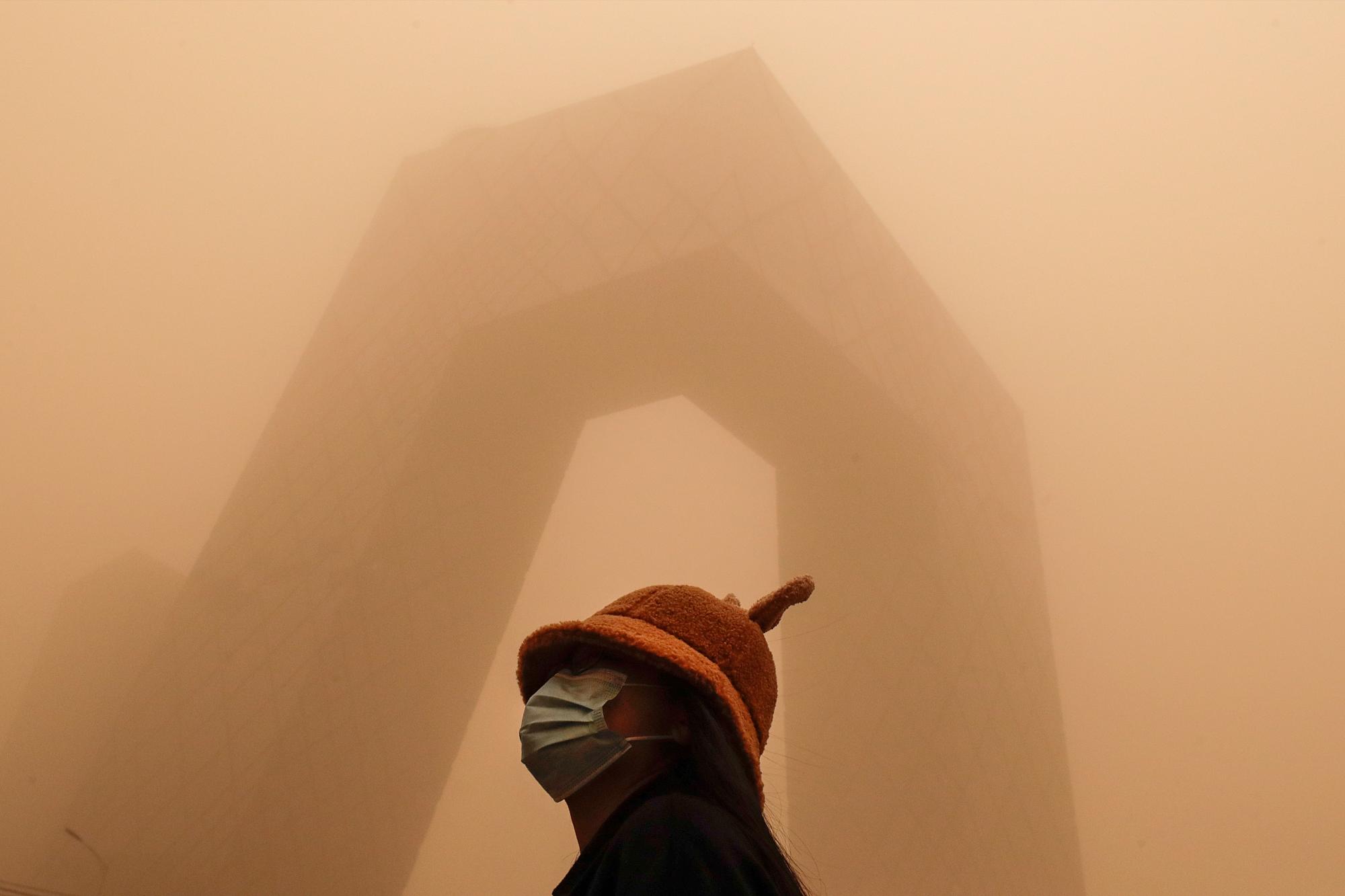 Una mujer que usa una mascarilla para ayudar a frenar la propagación del coronavirus se opone al edificio de la Televisión Central de China (CCTV) mientras la ciudad capital es golpeada por aire contaminado y una tormenta de arena en Beijing, el lunes 15 de marzo de 2021. neblina a los cielos de Beijing y envió índices de calidad del aire disparados el lunes. (AP Photo/Andy Wong)