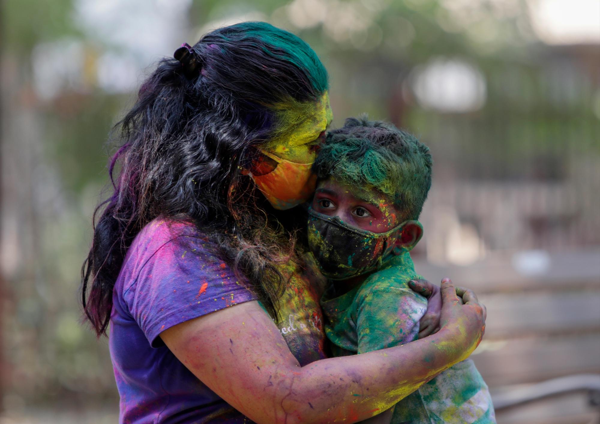 Una mujer india manchada de colores y con una máscara abraza a su hijo durante las celebraciones del festival Holi en Mumbai, India, el lunes 29 de marzo de 2021.Los hindúes arrojaron polvos de colores y rociaron agua en las celebraciones masivas de Holi el lunes a pesar de que muchos estados indios restringieron las reuniones para tratar de contener un resurgimiento del coronavirus en todo el país.