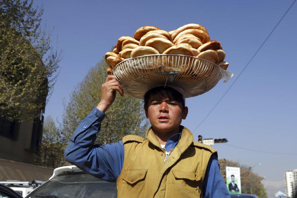 Un joven afgano porta panes dulces sobre su cabeza usando la rejilla de un abanico en Kabul, Afganistan, (AP Photo/Rahmat Gul)