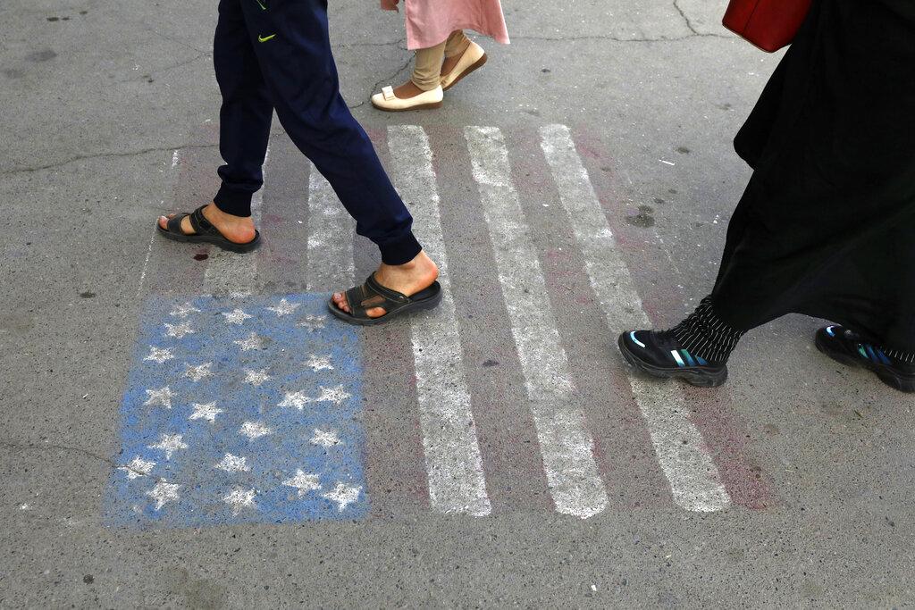 Varias personas caminan sobre una representación de la bandera de Estados Unidos que está pintada sobre el asfalto de la calle que conduce al templo de Saint Jafar, en el pueblo de Pishva al sur de Teherán, en Irán.  (AP Photo/Vahid Salemi)