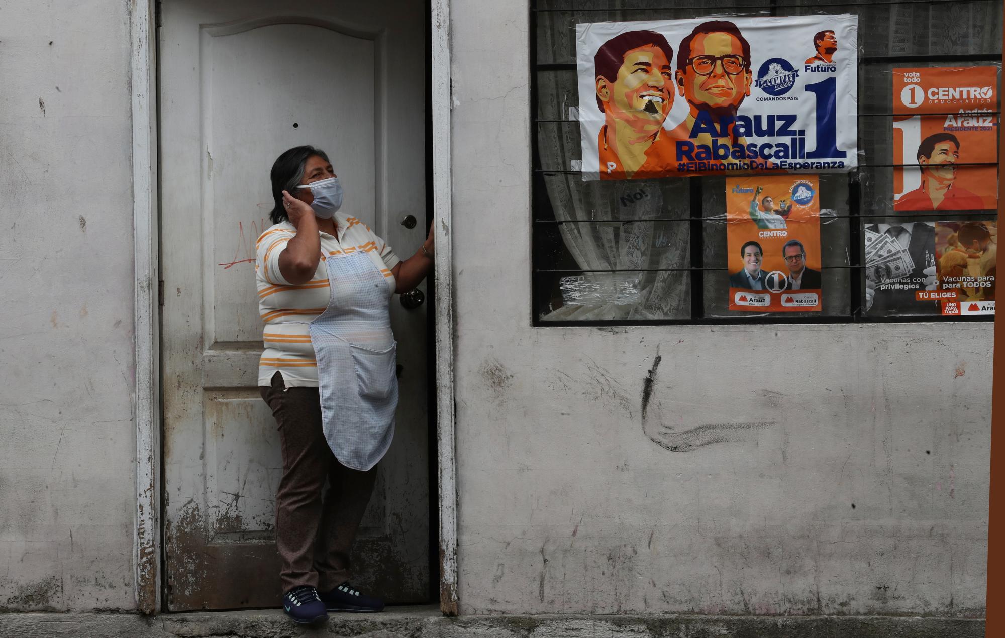 Una mujer se asoma por la puerta de su casa, una de cuyas ventanas muestra propaganda a favor del candidato presidencial Andrés Arauz de la Unión por la Esperanza (UNES), en Quito, Ecuador, el viernes 9 de abril de 2021. 