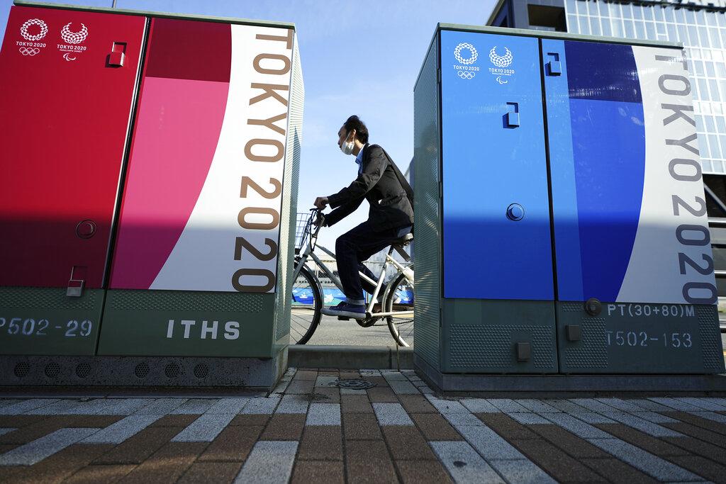 Un hombre que usa una mascarilla pasa detrás de dos avisos publicitarios que anuncian los Juegos Olímpicos y Paralímpicos Tokio 2020, que vuelven a estar bajo amenaza de suspensión.  (AP Photo/Eugene Hoshiko)
