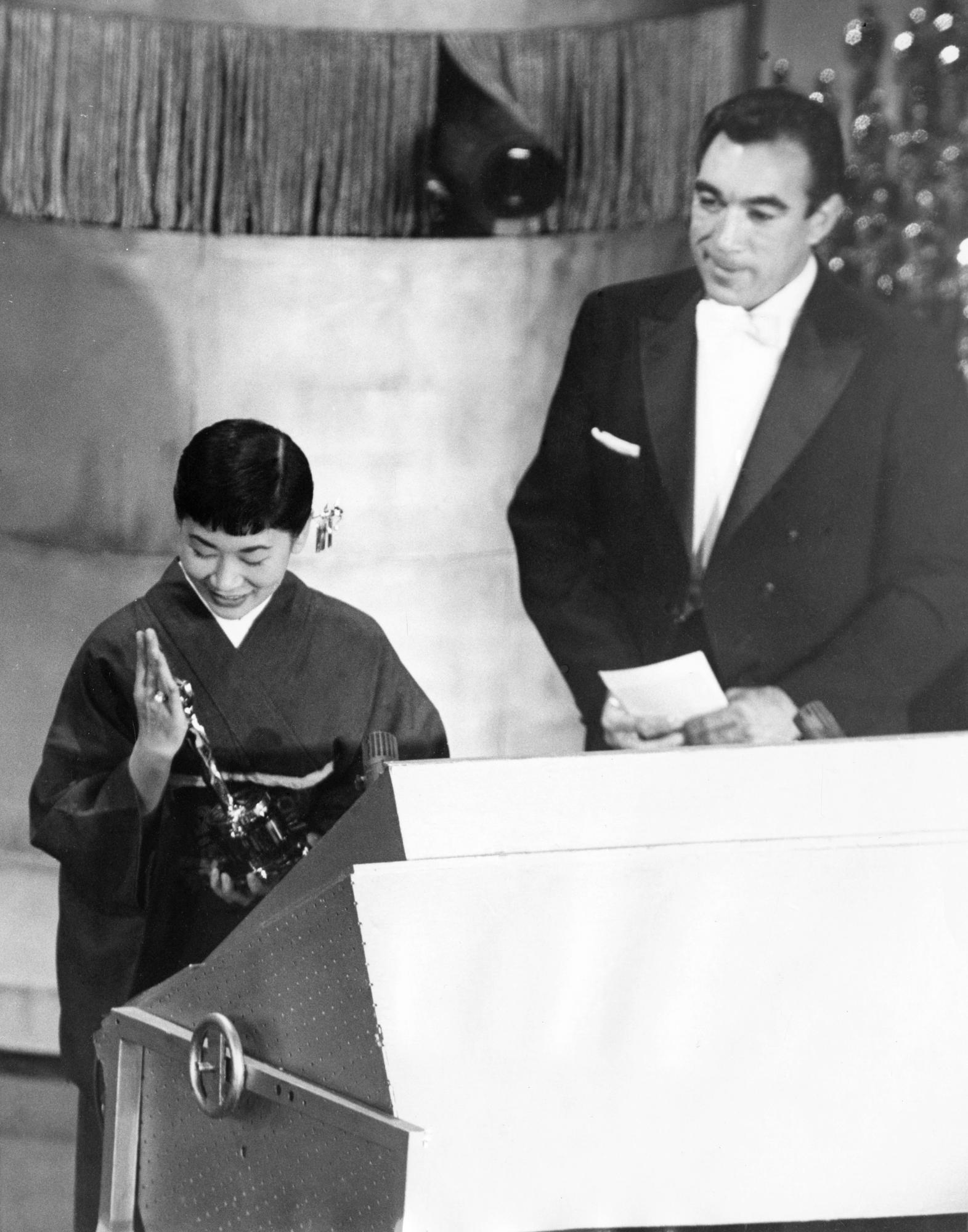 La actriz japonesa Miyoshi Umeki recibe el Premio de la Academia a mejor actriz de reparto por su papel en Sayonara, mientras el presentador Anthony Quinn la mira en los Premios de la Academia en Los Angeles el 26 de marzo de 1958. Umeki es la primera persona de Japón en ganar un Oscar.