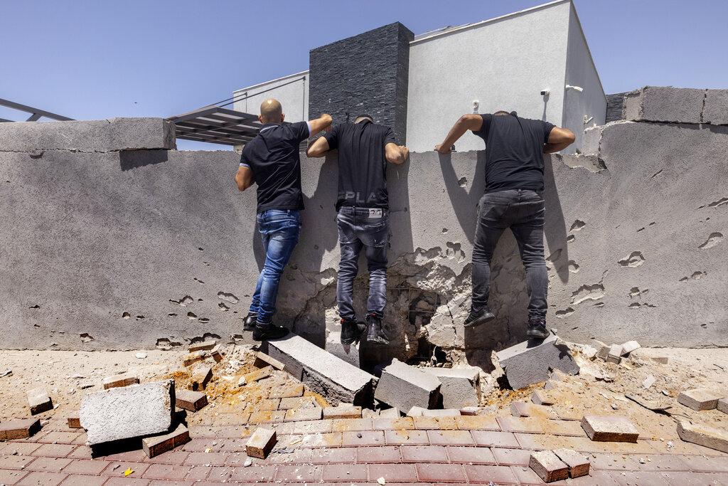 Tres hombres observan los daños causados por un cohete disparado desde la Franja de Gaza, en la ciudad de Ashkelon al sur de Israel. (AP Photo/Tsafrir Abayov)
