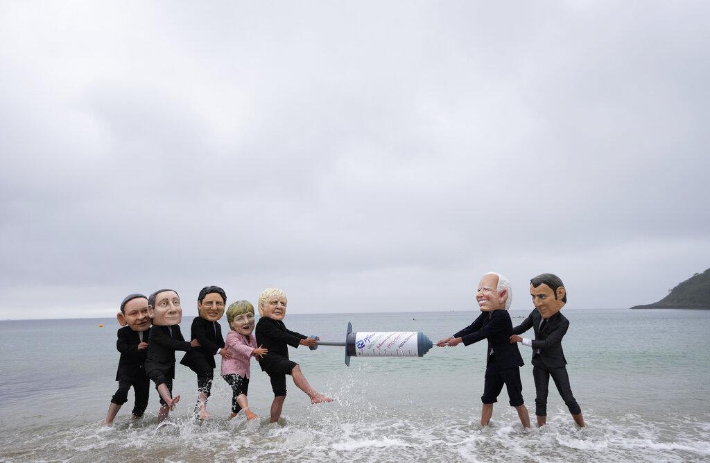 Activistas con cabezas gigantes de los líderes del G7 se pelean por una jeringa gigante de vacuna COVID-19 durante una acción de ONG en Swanpool Beach en Falmouth, Cornwall (Foto AP / Kirsty Wigglesworth)