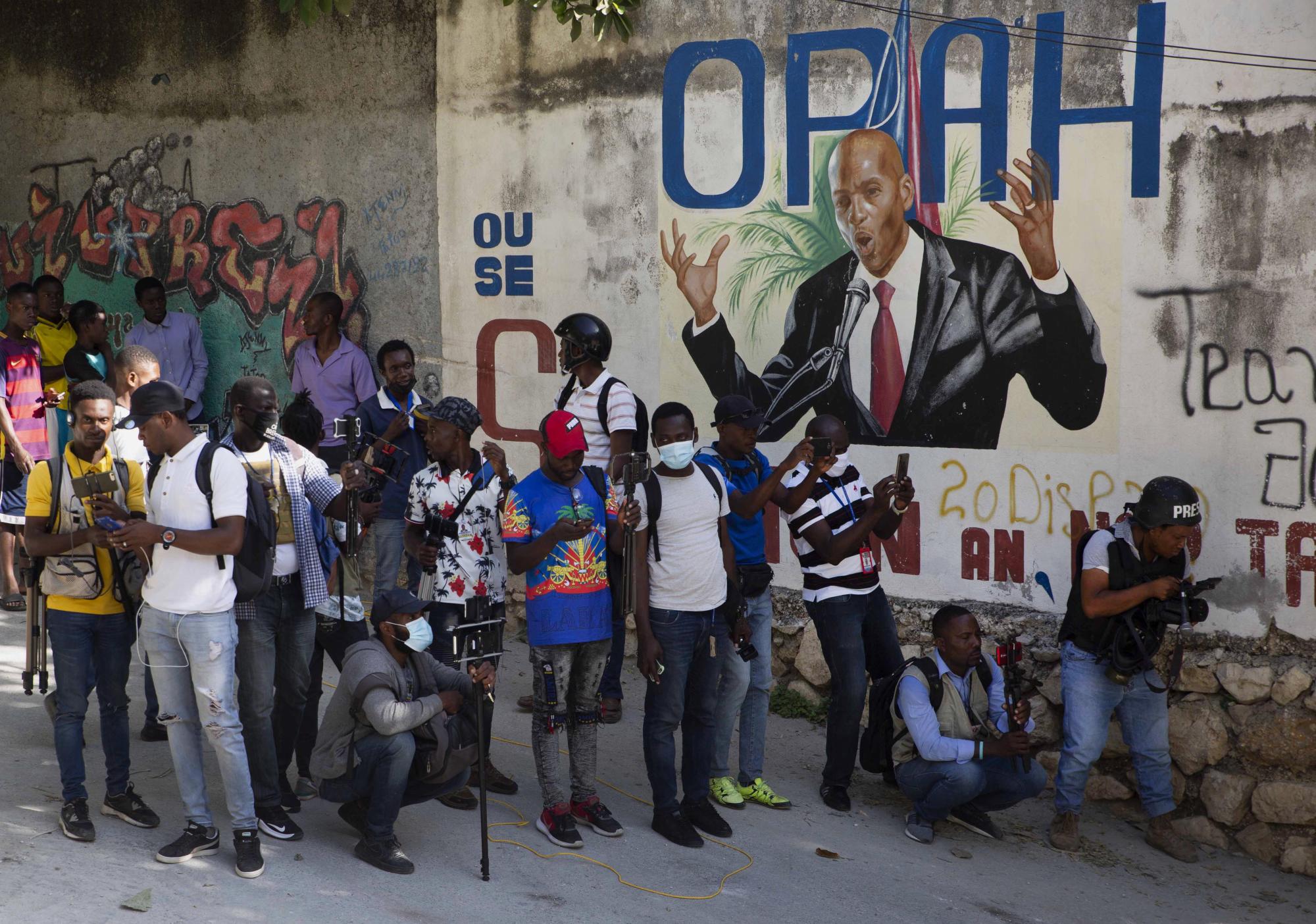 Periodistas se reúnen cerca de un mural que muestra al presidente haitiano Jovenel Moise, cerca de la residencia del líder, donde fue asesinado por hombres armados. Claude Joseph, el primer ministro interino, confirmó el asesinato y dijo que la policía y el ejército tenían el control de la seguridad en Haití. (Foto AP / Joseph Odelyn)