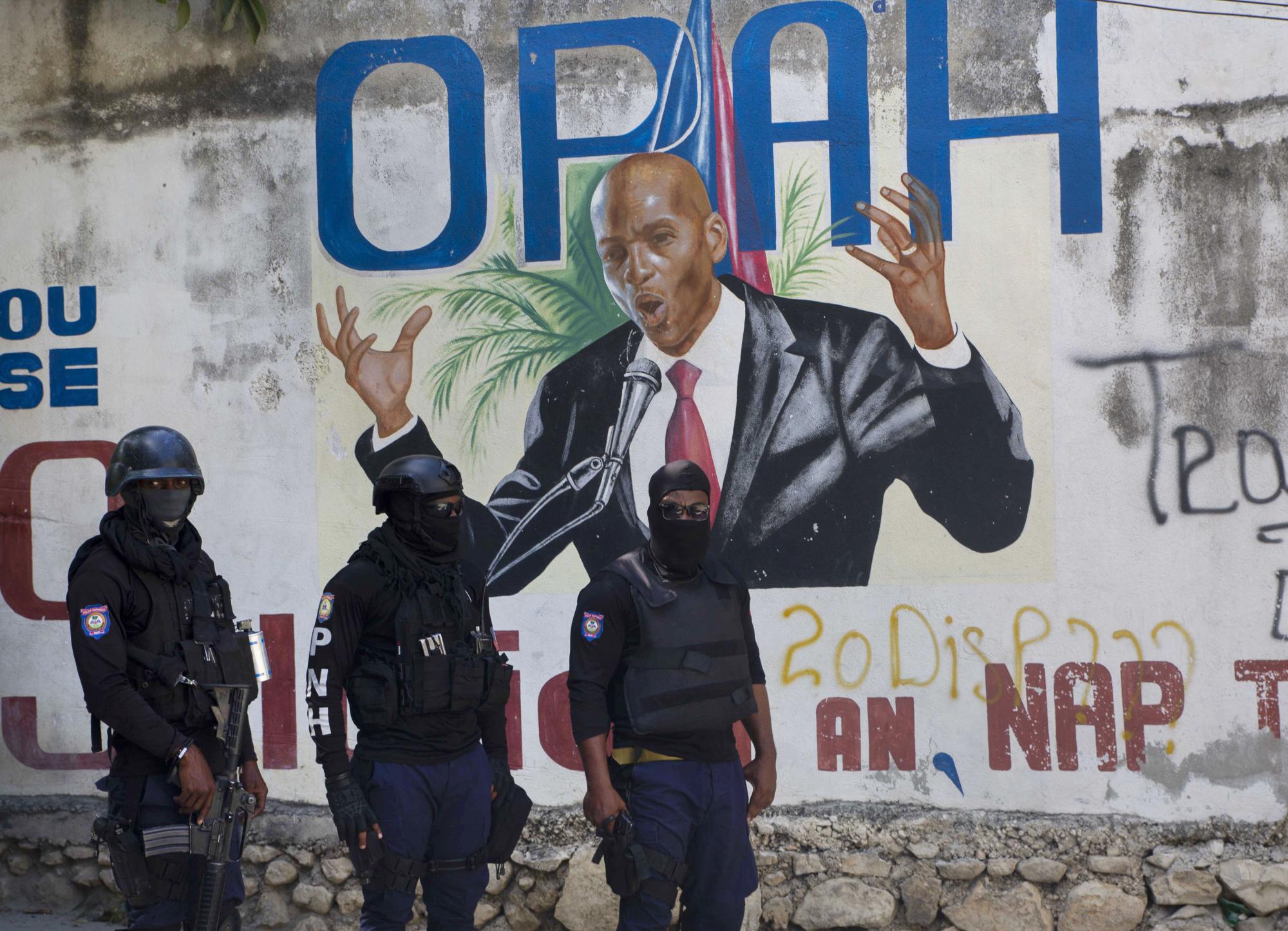 La policía se para cerca de un mural que muestra al presidente haitiano Jovenel Moise, cerca de la residencia del líder donde fue asesinado por hombres armados en las primeras horas de la mañana en Port-au-Prince, Haití, el miércoles 7 de julio de 2021. (AP Photo / Joseph Odelyn)