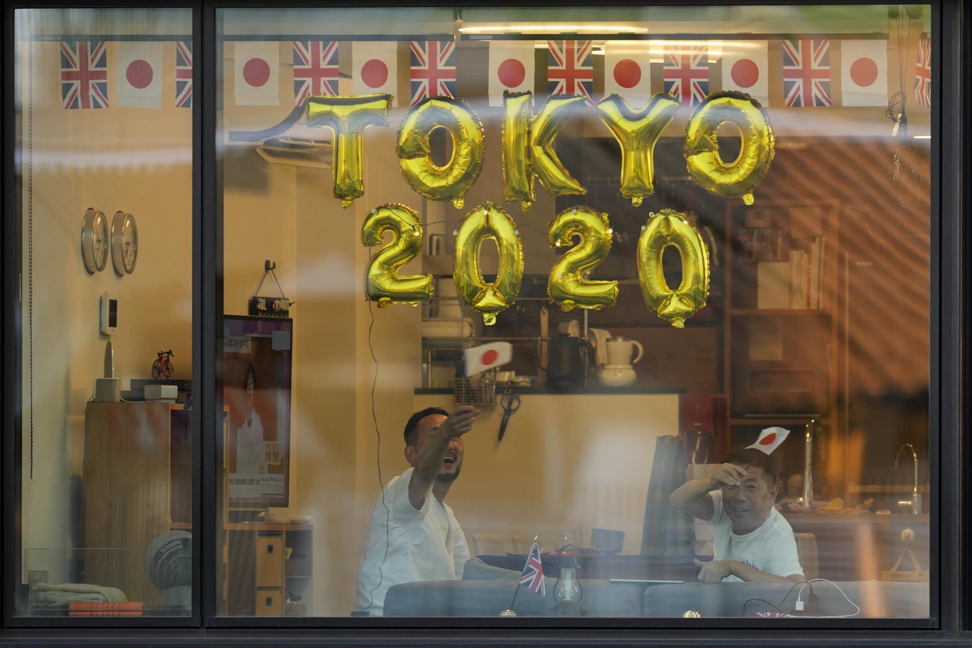 La gente mira por la ventana de su apartamento desde un edificio cercano antes de la ceremonia de apertura en el Estadio Olímpico de los Juegos Olímpicos de Verano de 2020, el viernes 23 de julio de 2021, en Tokio, Japón. (Foto AP / Lee Jin-man)