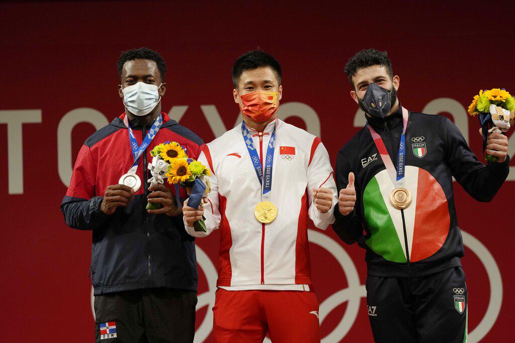 El medallista de oro Lyu Xiaojun de China, centro está flanqueado por el medallista de plata Zacarias Bonnat Michel de República Dominicana, izquierda, y el medallista de bronce Antonino Pizzolato de Italia, en el podio del evento de levantamiento de pesas masculino de 81 kg, en los Juegos Olímpicos de Verano de 2020, sábado 31 de julio. , 2021, en Tokio, Japón. (Foto AP / Luca Bruno)