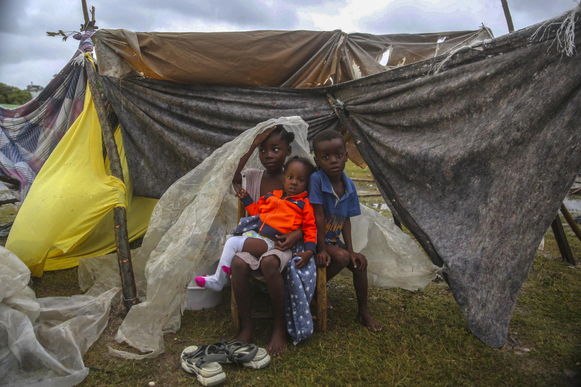 Los niños desplazados por el terremoto se apiñan debajo de una pieza de plástico la mañana después de que la tormenta tropical Grace barrió Les Cayes, Haití, el martes 17 de agosto de 2021, tres días después de un terremoto de magnitud 7.2. (Foto AP / Joseph Odelyn)