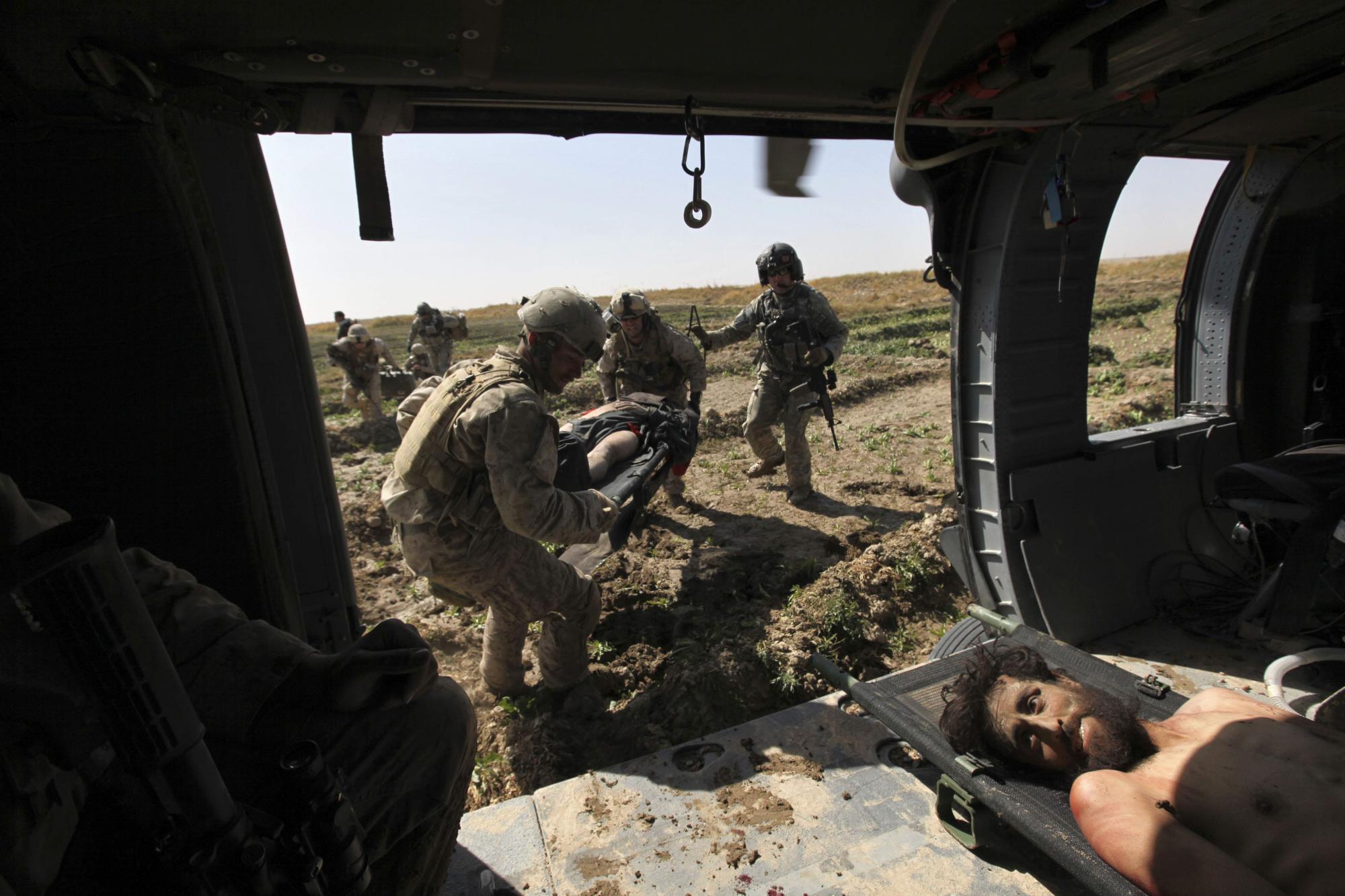 Durante un tiroteo esporádico, el Sargento del Ejército de Estados Unidos. y el médico de vuelo Robert B. Cowdrey, de La Junta, Colorado, arriba a la derecha, con la Fuerza de Tarea Pegasus, coordina una misión de evacuación médica mientras los infantes de marina llevan en un helicóptero el segundo de dos combatientes talibanes heridos capturados minutos antes, según testigos. en Marjah, provincia de Helmand, Afganistán, miércoles 17 de febrero de 2010. (Foto AP / Brennan Linsley)