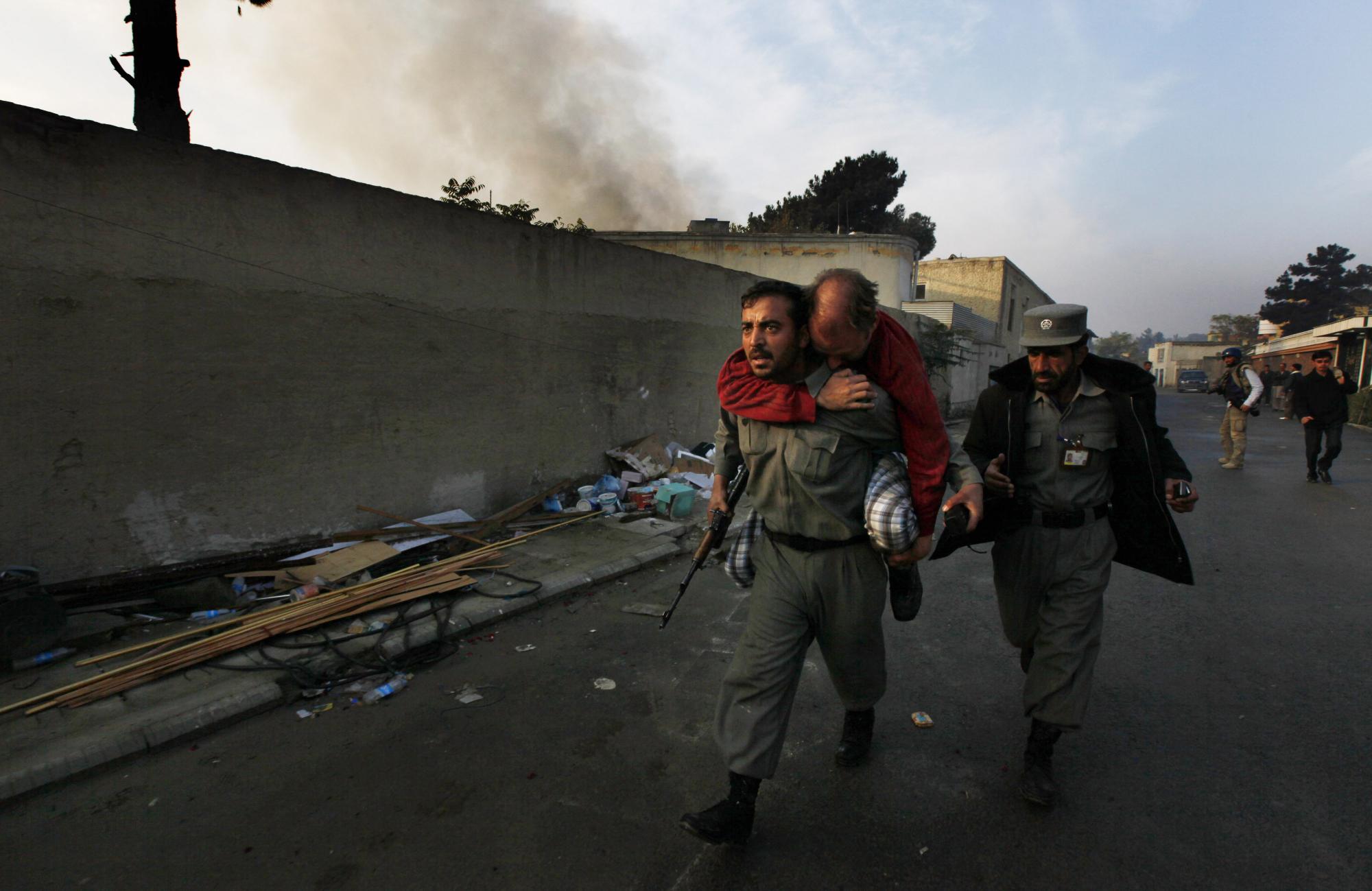 Un oficial de policía afgano transporta a un ciudadano alemán no identificado herido mientras el humo sale del lugar de un ataque en Kabul, Afganistán, el miércoles 28 de octubre de 2009. Hombres armados atacaron una casa de huéspedes utilizada por personal de la ONU en la capital afgana de Kabul. (Foto AP / Gemunu Amarasinghe)
