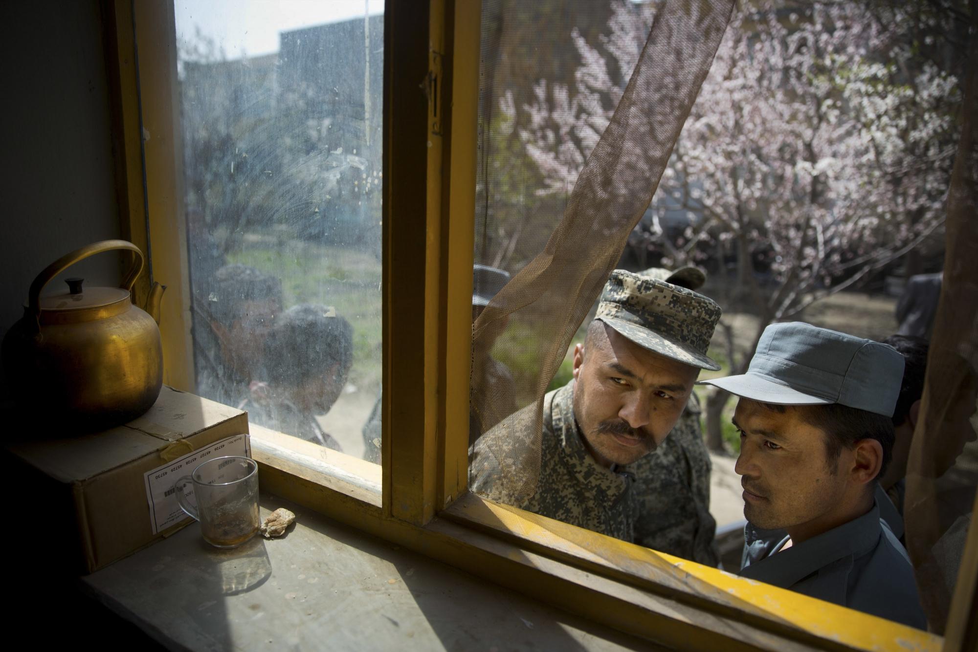 Un soldado afgano, a la izquierda, y un policía se asoman a través de una ventana mientras hacen cola con otros para obtener su tarjeta de registro el último día de registro de votantes para las próximas elecciones presidenciales frente a una escuela en Kabul, Afganistán, el martes 1 de abril de 2014 (Foto AP / Anja Niedringhaus)
