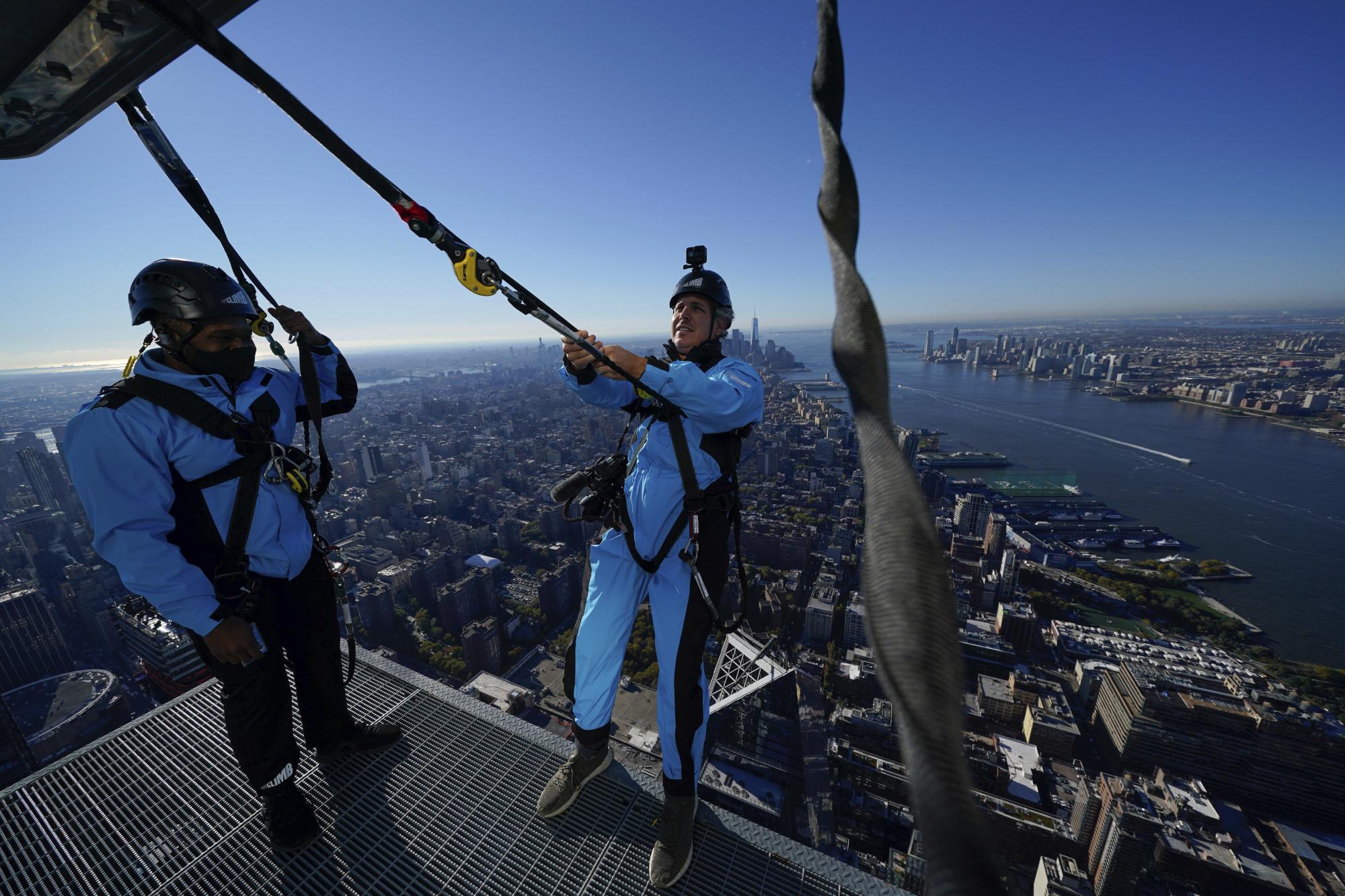 El videoperiodista David Martin, a la derecha, se inclina hacia atrás sobre el borde de City Climb, una nueva atracción en 30 Hudson Yards en Nueva York, el miércoles 3 de noviembre de 2021. (Foto AP / Seth Wenig)