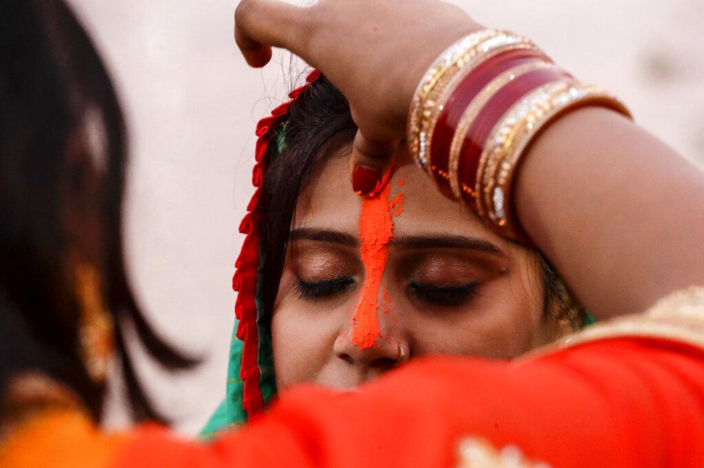 Una mujer hindú pone bermellón en la frente de otra a orillas del río Hooghly temprano en la mañana durante el festival Chhath, en Calcuta, India, el jueves 11 de noviembre de 2021. Durante el Chhath, un antiguo festival hindú, se realizan rituales para agradecer al sol dios por sostener la vida en la tierra. (Foto AP / Bikas Das)