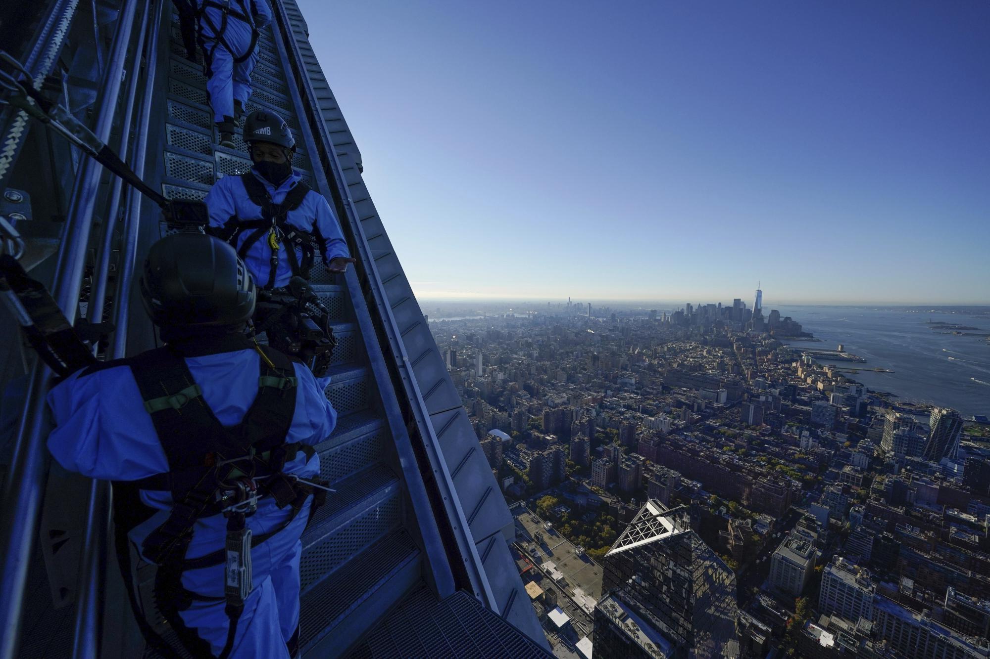 Personal de la excursión City Climb instruye a un grupo de periodistas que escalan la parte exterior del edificio en 30 Hudson Yards, sujetados por arneses conectados a rieles, el 3 de noviembre del 2021. (AP Photo/Seth Wenig)