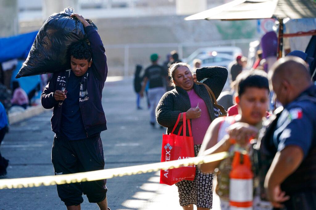 Migrantes cargan con sus pertenencias en un asentamiento improvisado que bloquea la entrada a un cruce peatonal a Estados Unidos (arriba), el 8 de noviembre de 2021, en Tijuana, México. El campamento, ahora rodeado por una cerca metálica tras una operación policial el 28 de octubre, sirve de alojamiento temporal a cientos de migrantes que esperan solicitar asilo en Estados Unidos.