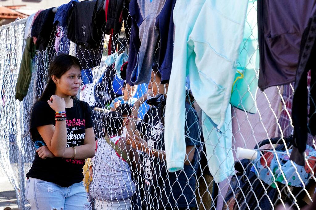 Migrantes hablan a través de la cerca de un asentamiento improvisado que bloquea la entrada a un cruce peatonal a Estados Unidos (arriba), el 8 de noviembre de 2021, en Tijuana, México. El campamento, ahora rodeado por una cerca metálica tras una operación policial el 28 de octubre, sirve de alojamiento temporal a cientos de migrantes que esperan solicitar asilo en Estados Unidos.