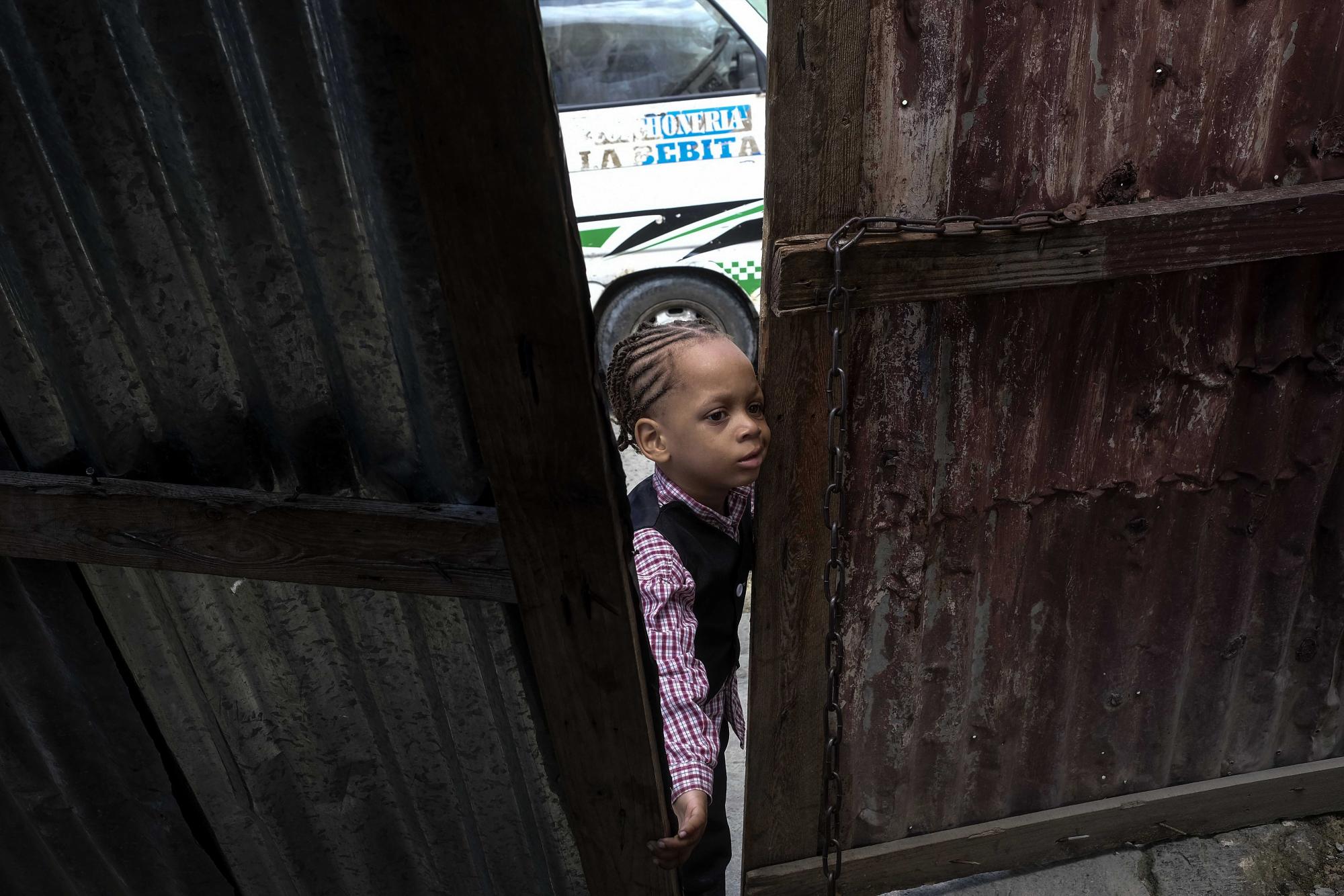 Un niño está parado en una puerta mientras espera a su madre en el barrio Los Coquitos en Santo Domingo, República Dominicana, el domingo 21 de noviembre de 2021. La comunidad empobrecida ha atraído a migrantes haitianos que buscan escapar de la mirada de las autoridades migratorias en ciudades más grandes. , donde dicen que también son blanco de delincuentes dominicanos. (Foto AP / Matias Delacroix)