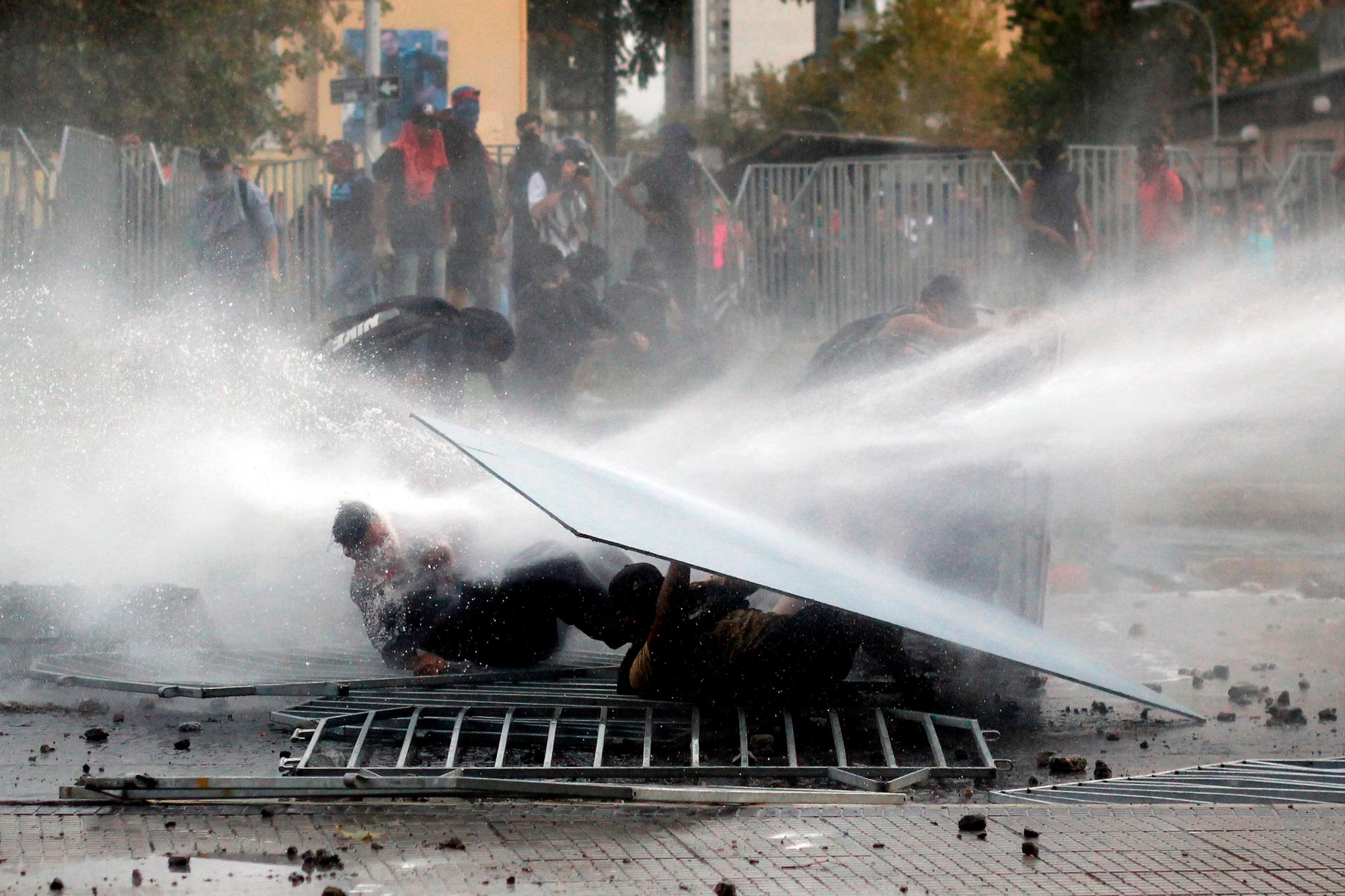 Manifestantes son alcanzados por el chorro de agua del camión de la policía antidisturbios hoy miércoles 11 de marzo, durante las protestas en conmemoración a los dos años de gobierno de Sebastián Piñera, en Santiago de Chile (Chile).