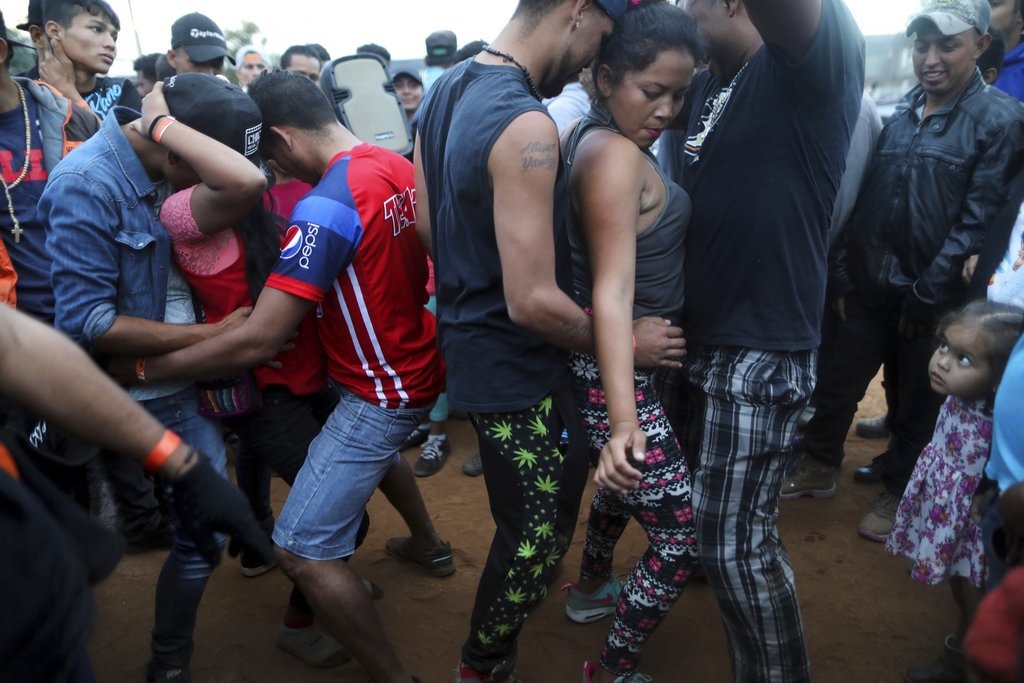 Migrantes centroamericanos bailan próximo a la barrera que separa a México de Estados Unidos.