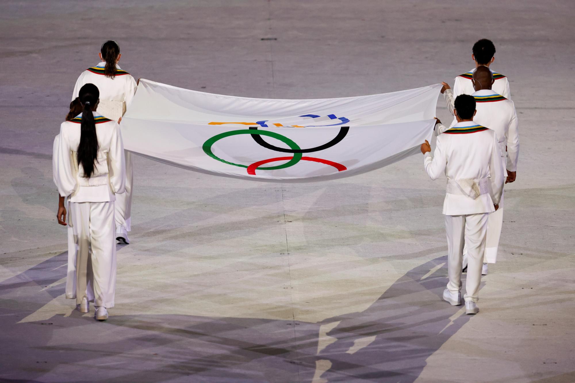 Operarios portan la Bandera Olímpica durante la ceremonia inaugural de los Juegos Olímpicos de Tokio 2020, este viernes en el Estadio Olímpico, que no contará con la presencia de público en las gradas. (EFE/Enric Fontcuberta)