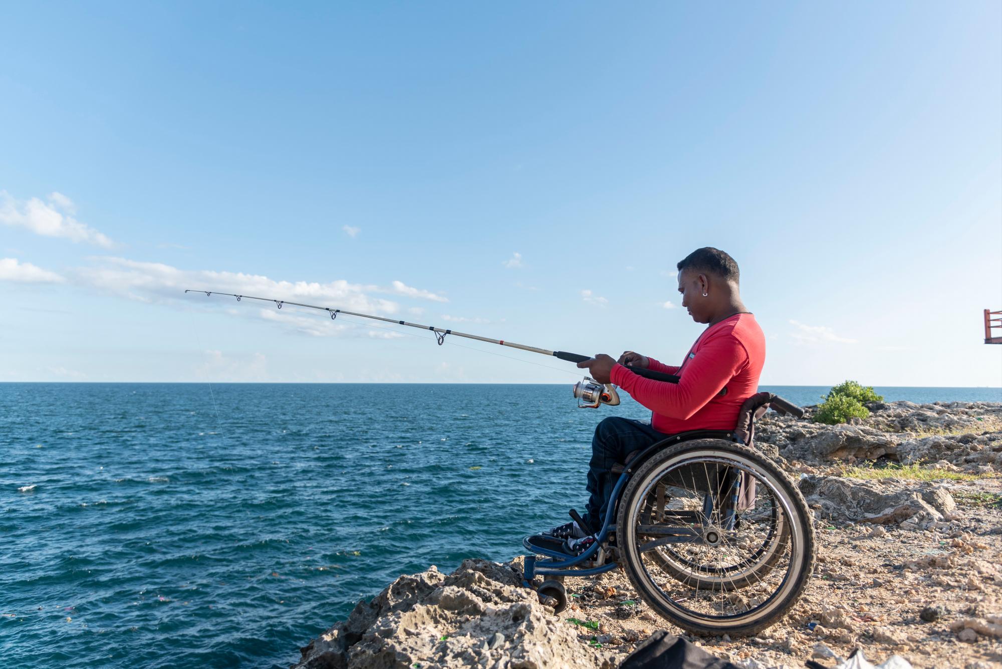 Un pescador en silla de ruedas disfruta del atardecer en el malecón de Santo Domingo