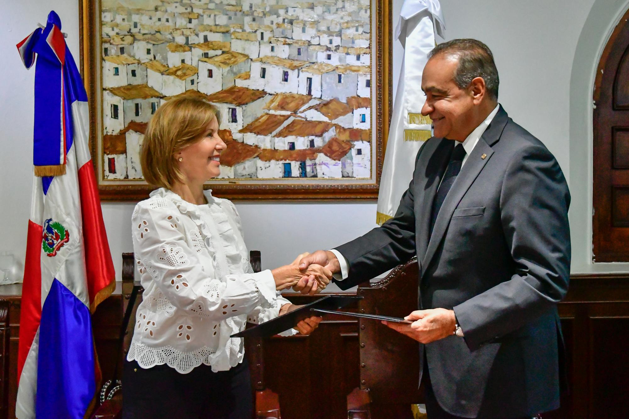 Rosangela Pellerano Peña de Elías y Julio Amado Castaños Guzmán intercambian las carpetas firmadas.