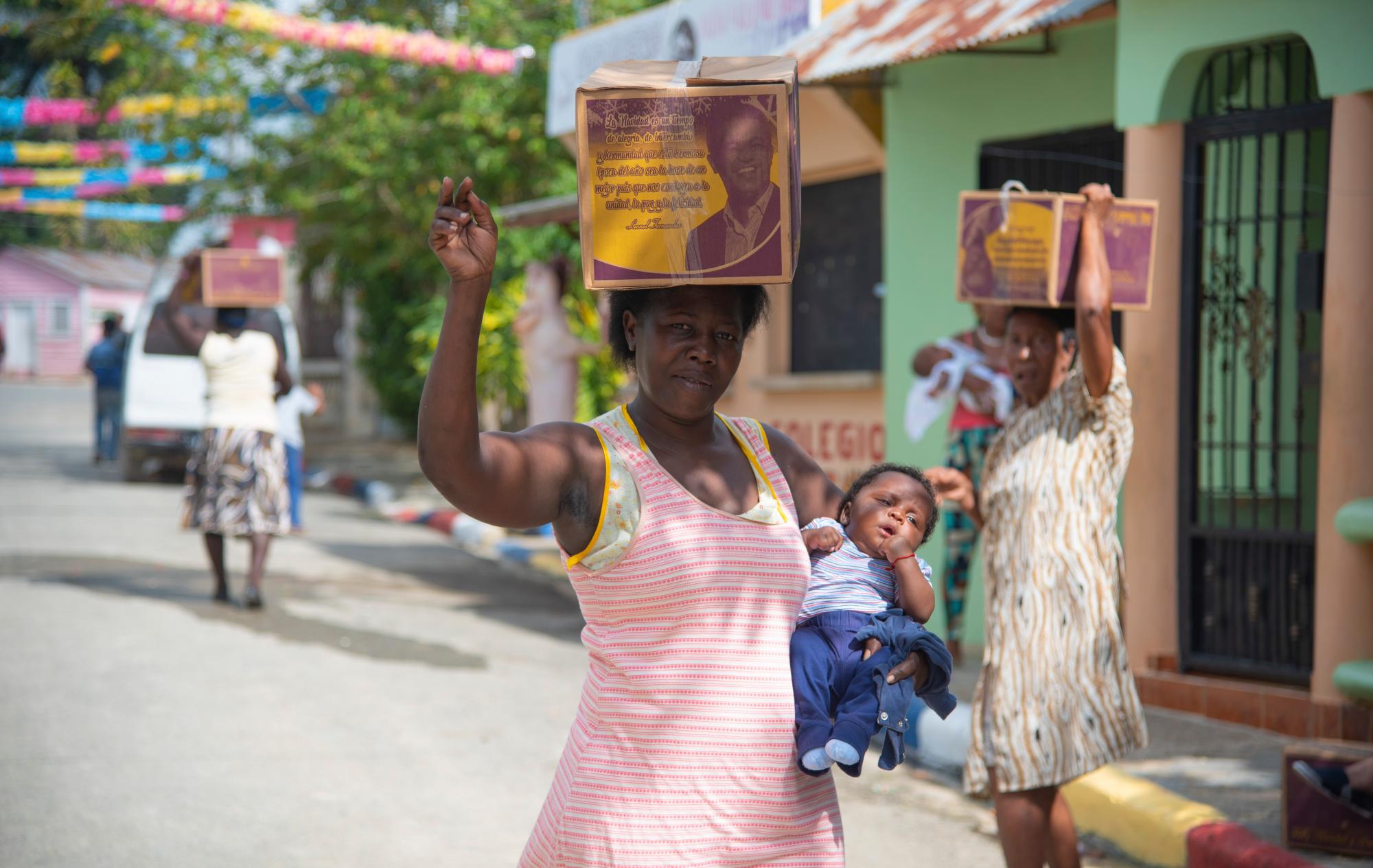 Una mujer pobre carga su pequeño hijo mientras sostiene una caja con la foto del expresidente Leonel Fernández.