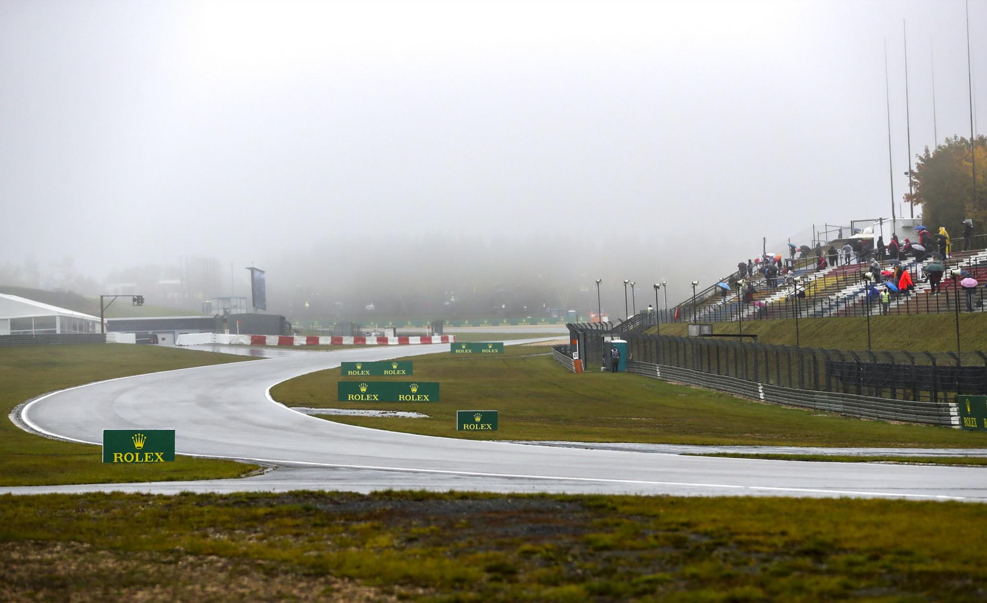 Los espectadores esperan en las gradas bajo la lluvia mientras el inicio de la primera sesión de entrenamientos se retrasa durante el Gran Premio de Eifel de Fórmula Uno. (EFE/Matthias Schrader)