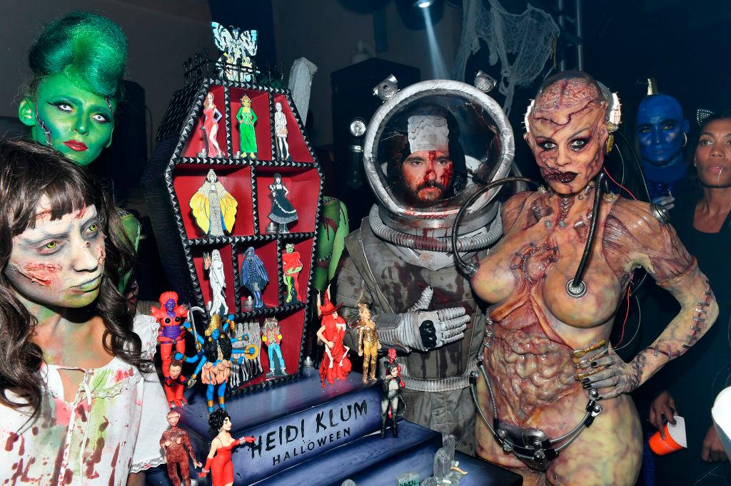 Tom Kaulitz y Heidi Klum posen ante representación en miniatura de todos sus disfraces anteriores.