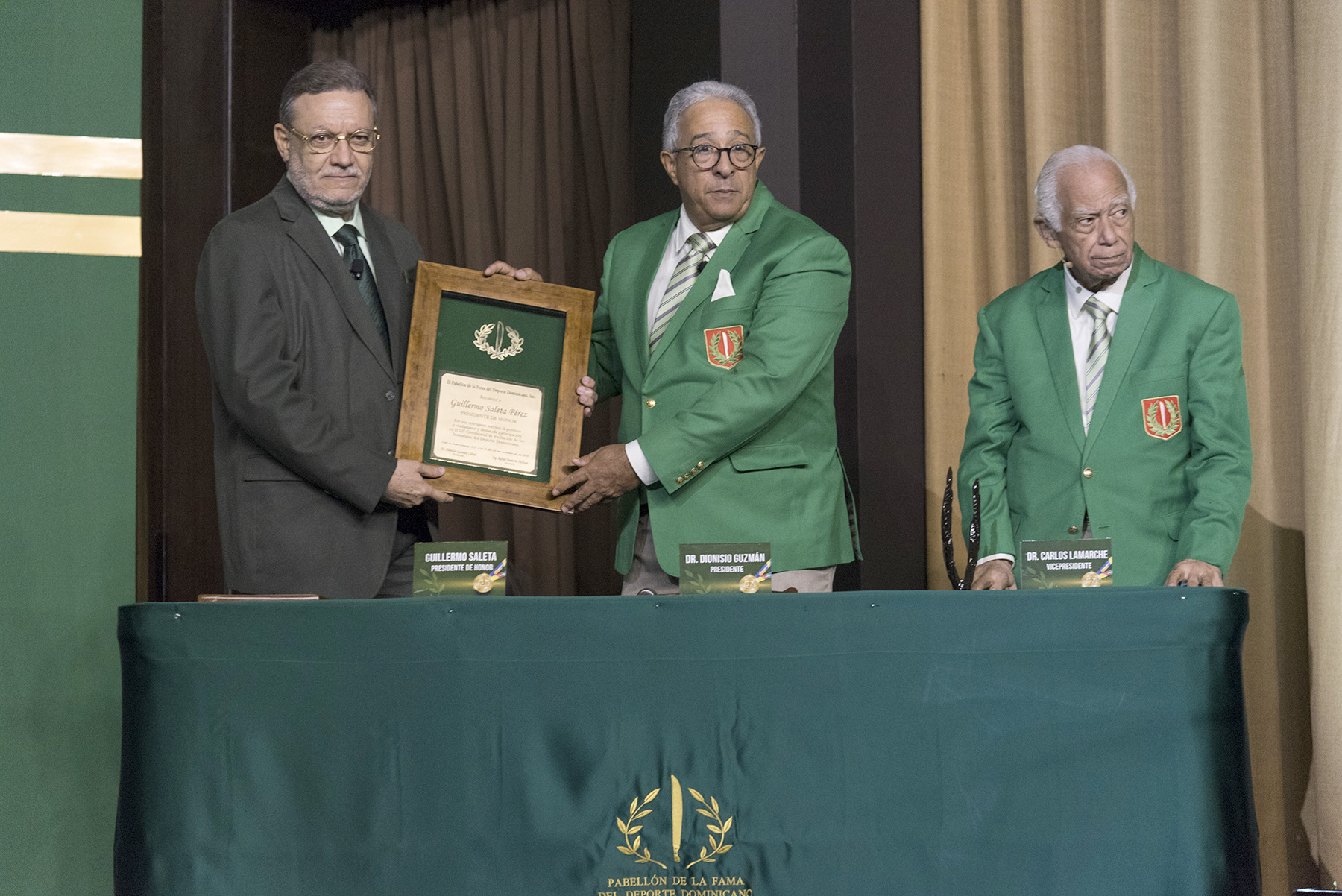 Guillermo Saleta recibe la placa, de manos del presidente del Comité Permanente del Pabellón de la Fama, Dionisio Guzmán, la cual lo acredita como miembro de ese comité. Saleta presidió el 52 ceremonial del domingo 11 de noviembre de 2018 en el Pabellón de la Fama del Deporte Dominicano.