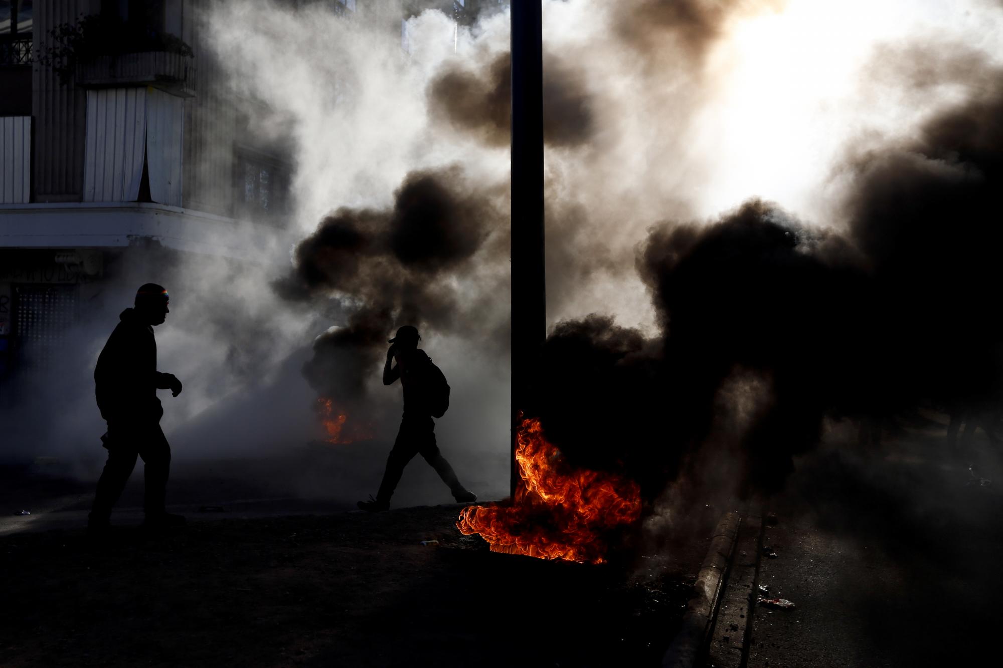 Manifestantes caminan a través del humo durante una protesta en el segundo aniversario del inicio de las protestas masivas contra el gobierno por la desigualdad, en Santiago, Chile, el lunes 18 de octubre de 2021. (AP Photo/Luis Hidalgo)