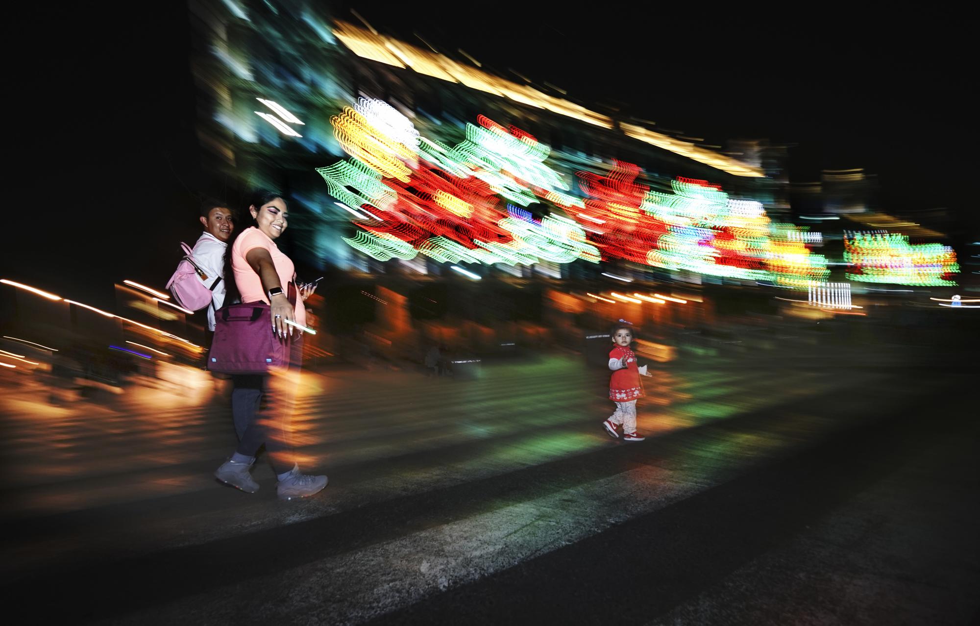 Una familia camina en la plaza principal de la Ciudad de México, el Zócalo, mientras brillan las luces navideñas. (AP)