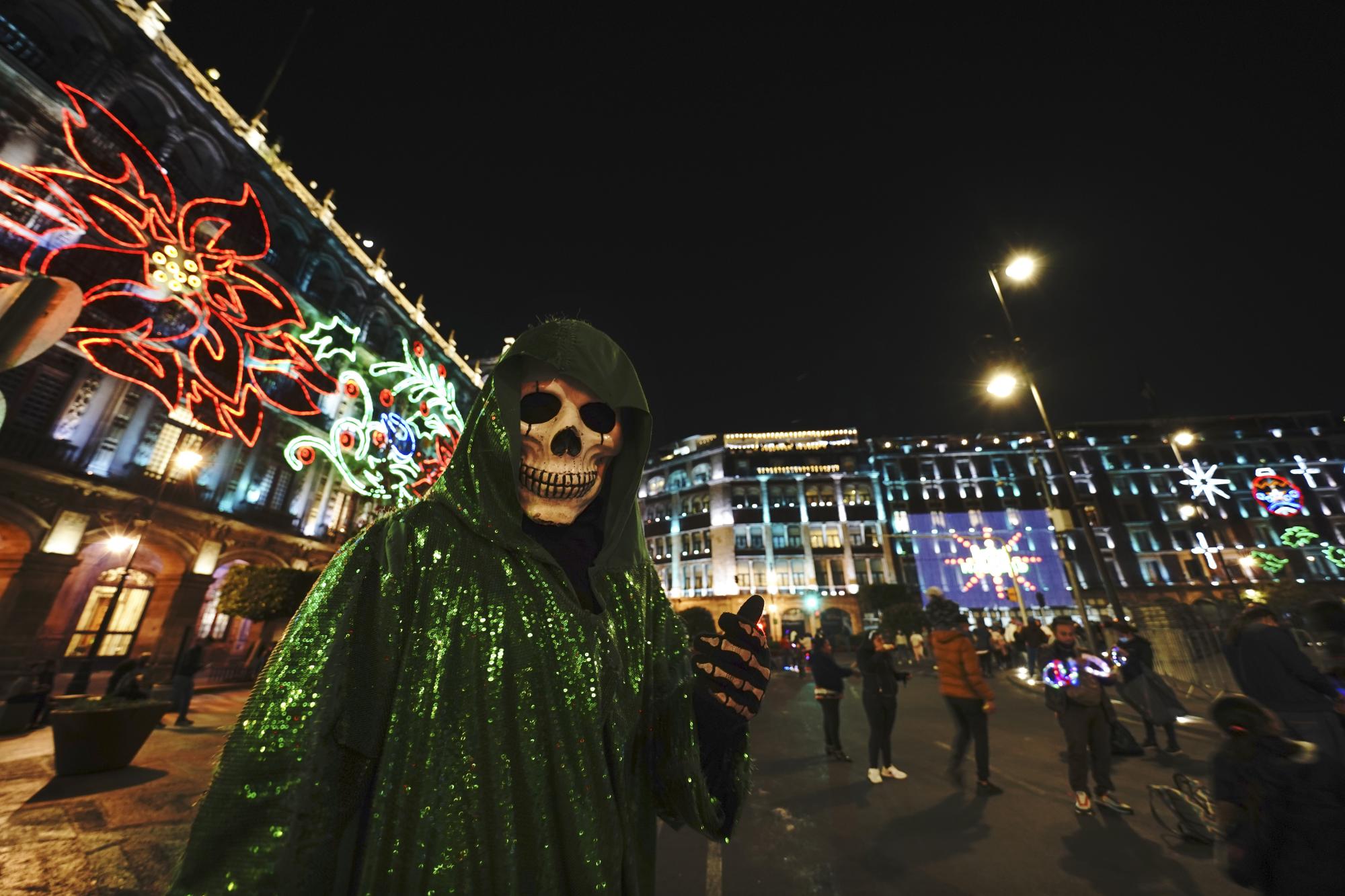 Una persona vestida de La Santa Muerte posa para una foto en la plaza principal de la Ciudad de México, el Zócalo, mientras brillan las luces navideñas. (AP)