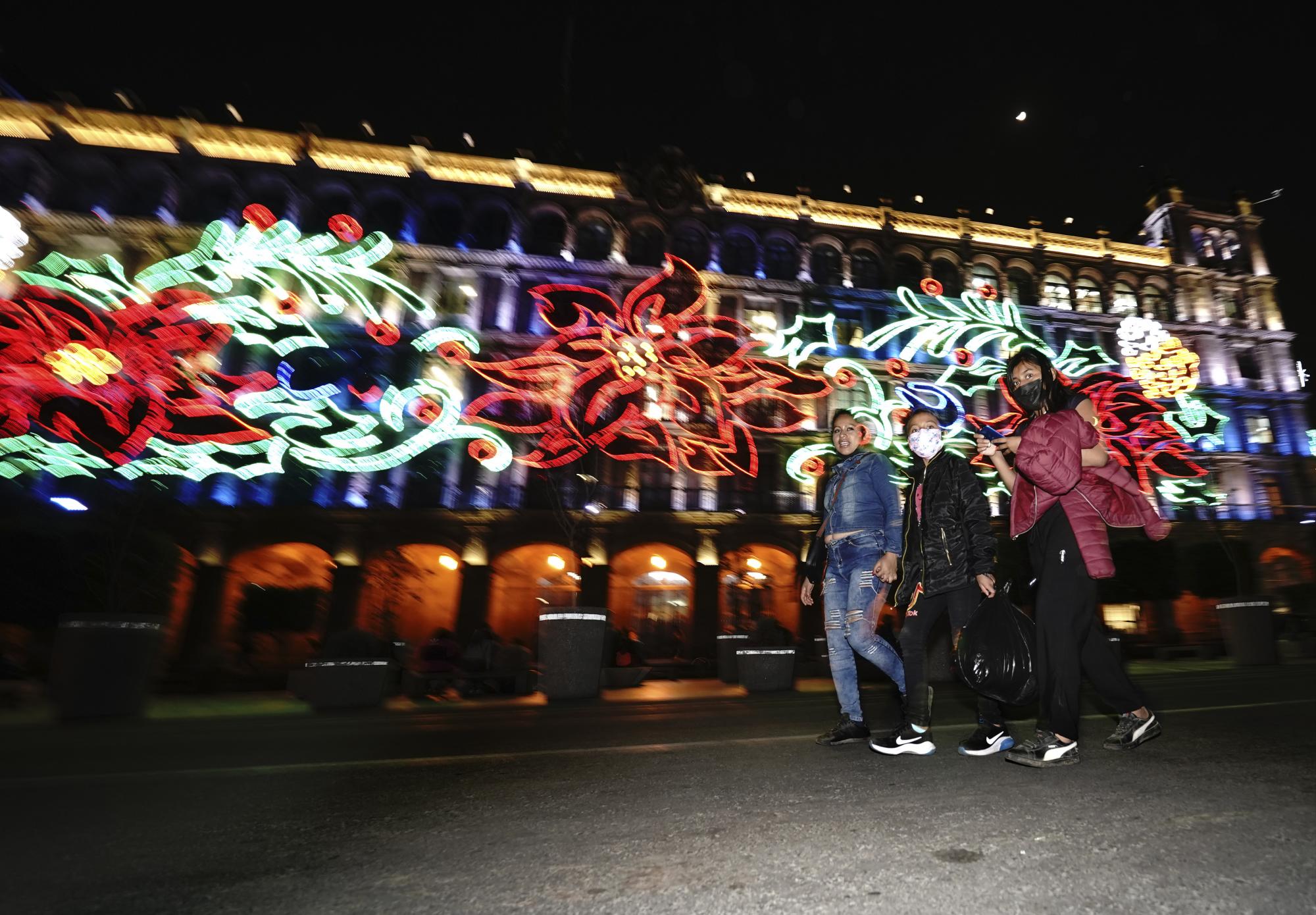 Jóvenes caminan en la plaza principal de la Ciudad de México, el Zócalo, mientras brillan las luces navideñas. (AP)