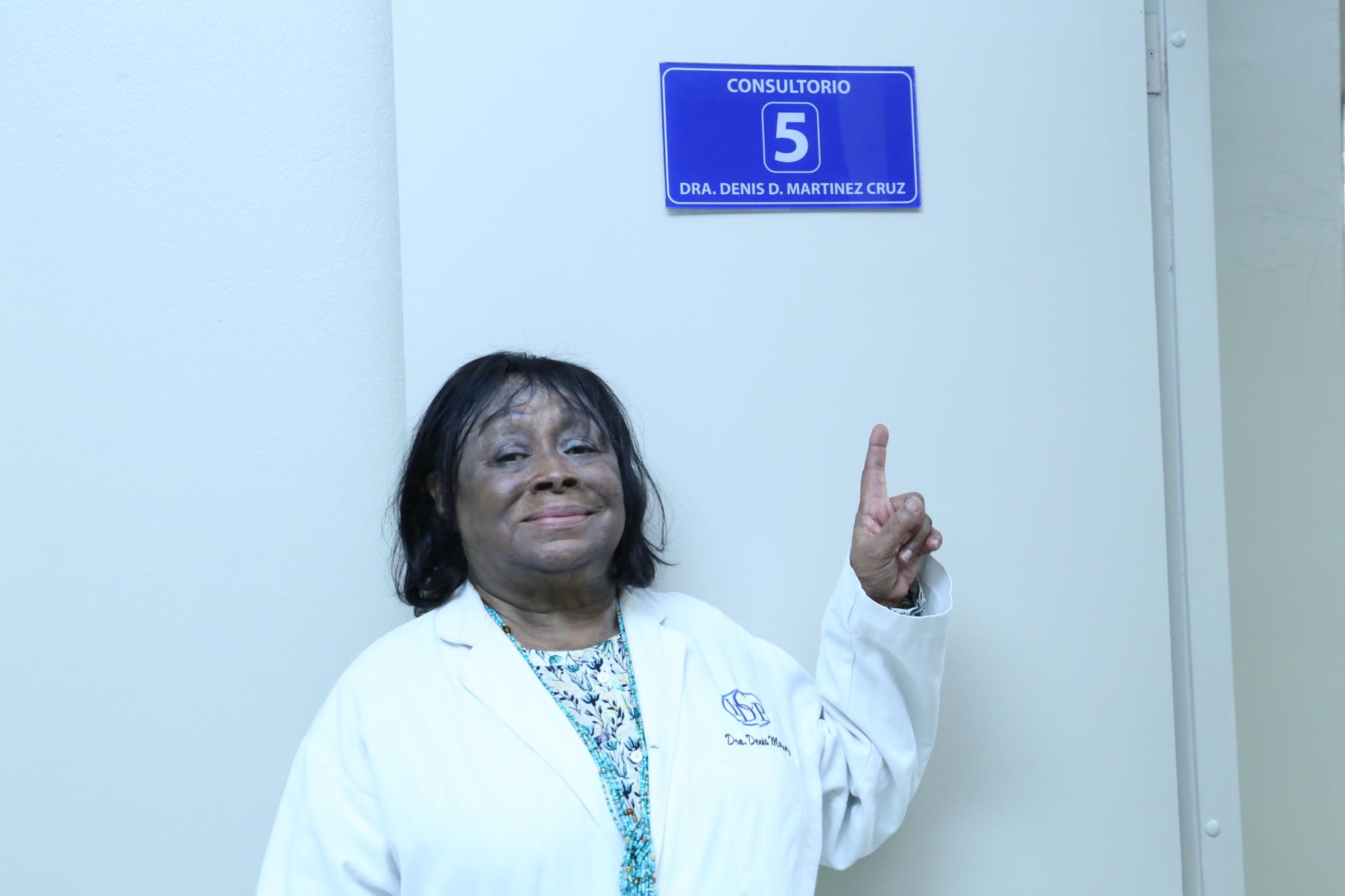La doctora Denis Martínez mientras señala el letrero colocado al consultorio que lleva su nombre en la sede principal del Instituto Dermatológico. (Fuente Externa) 